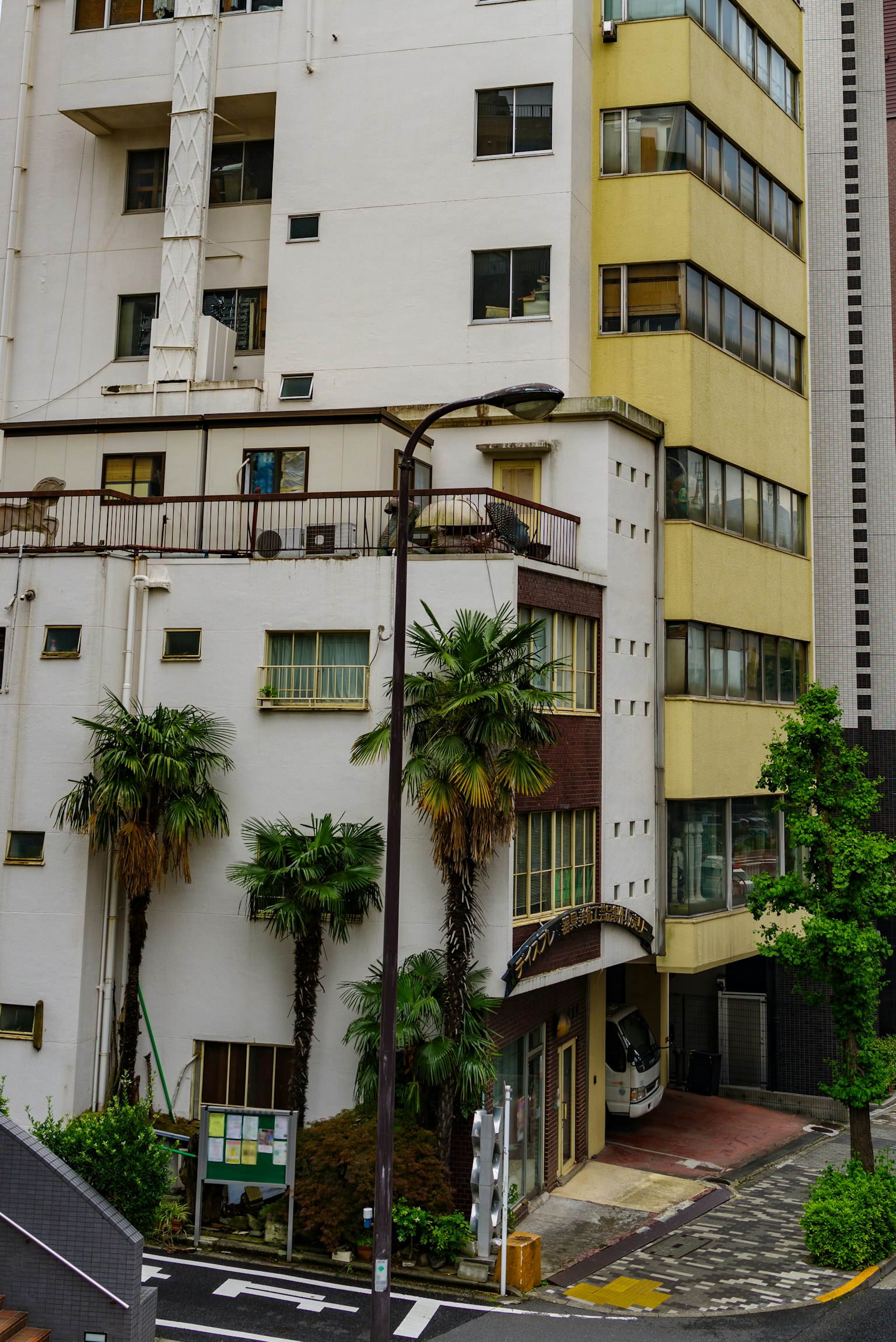 Esquina de la calle con un edificio blanco y amarillo que presenta palmeras y una calle pavimentada