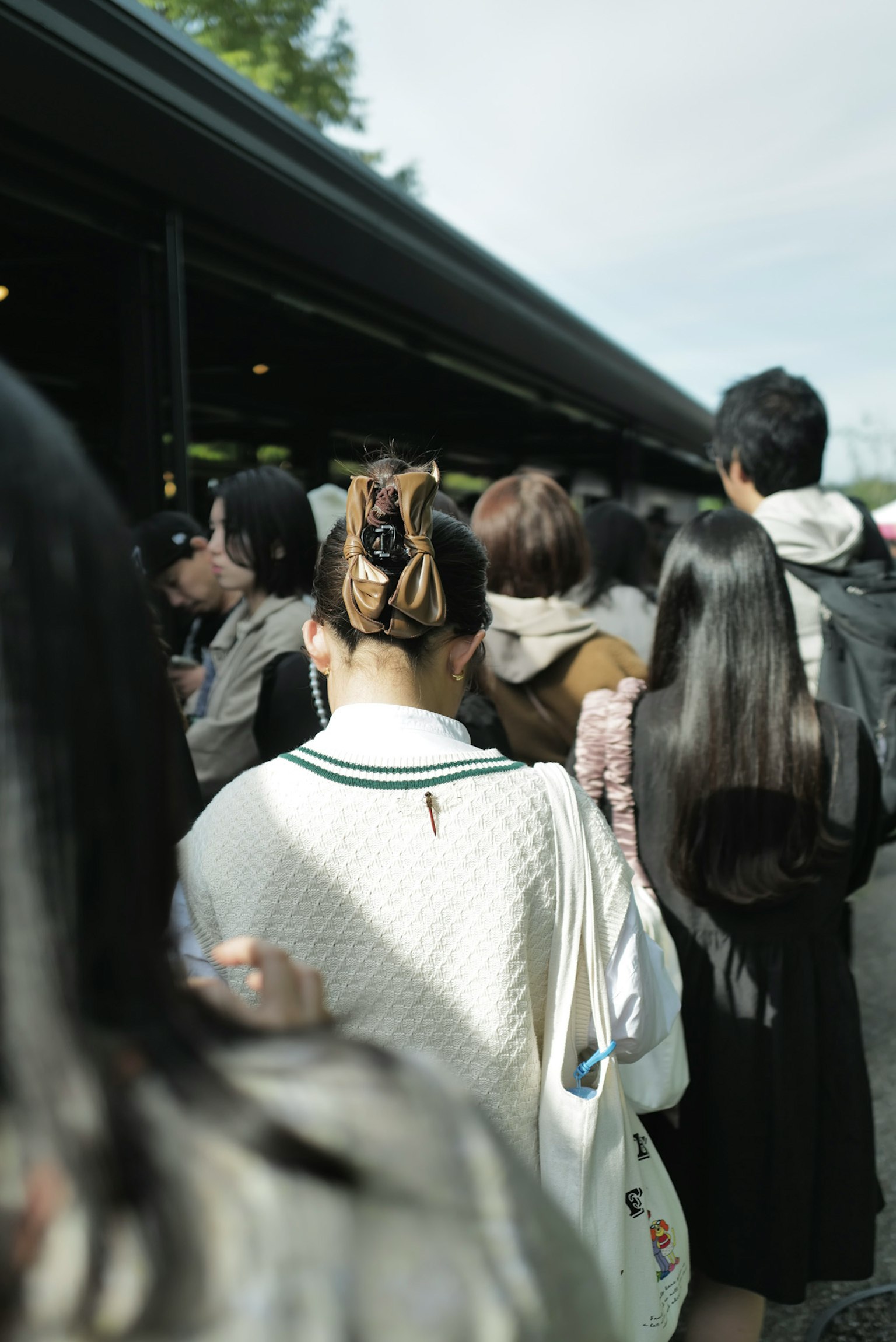 人々が並んでいる様子が見える画像 後ろ姿の女性が白いセーターを着ている