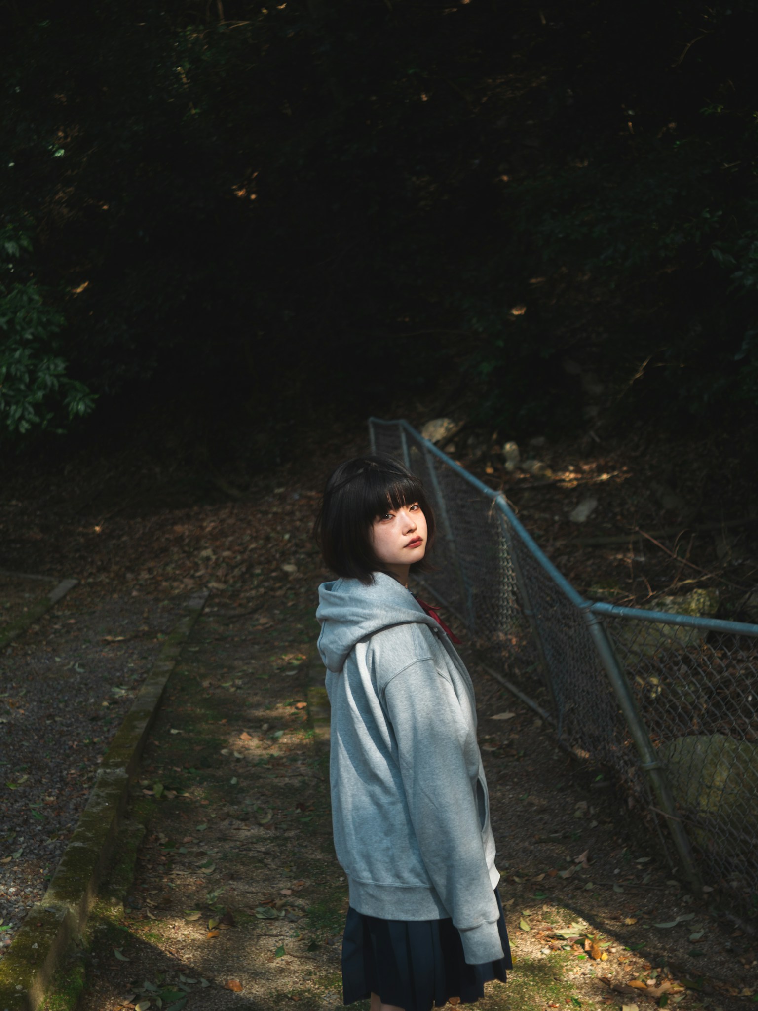 Girl in gray hoodie looking back in a forest setting