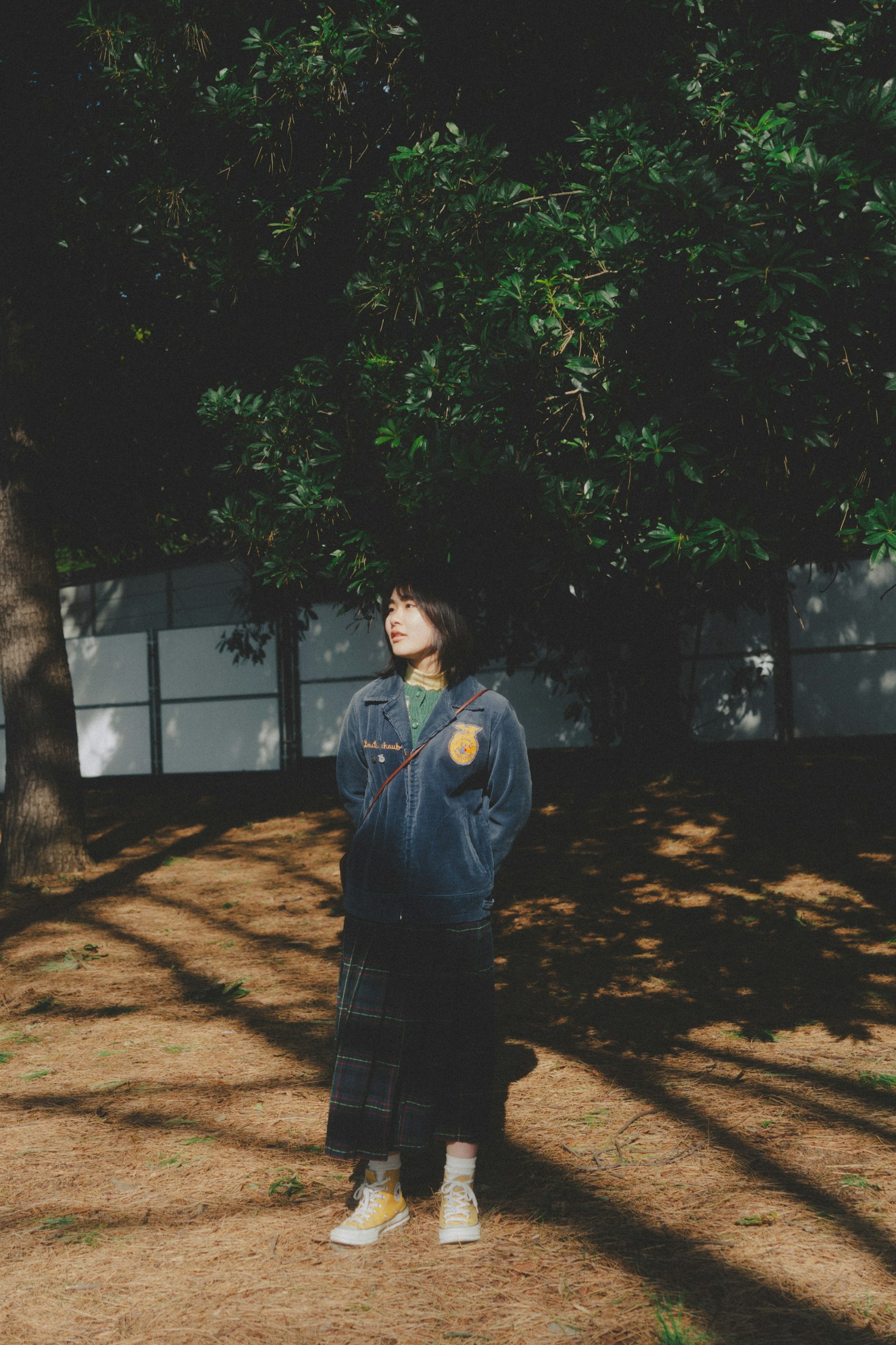 Person standing under green trees casual outfit natural light