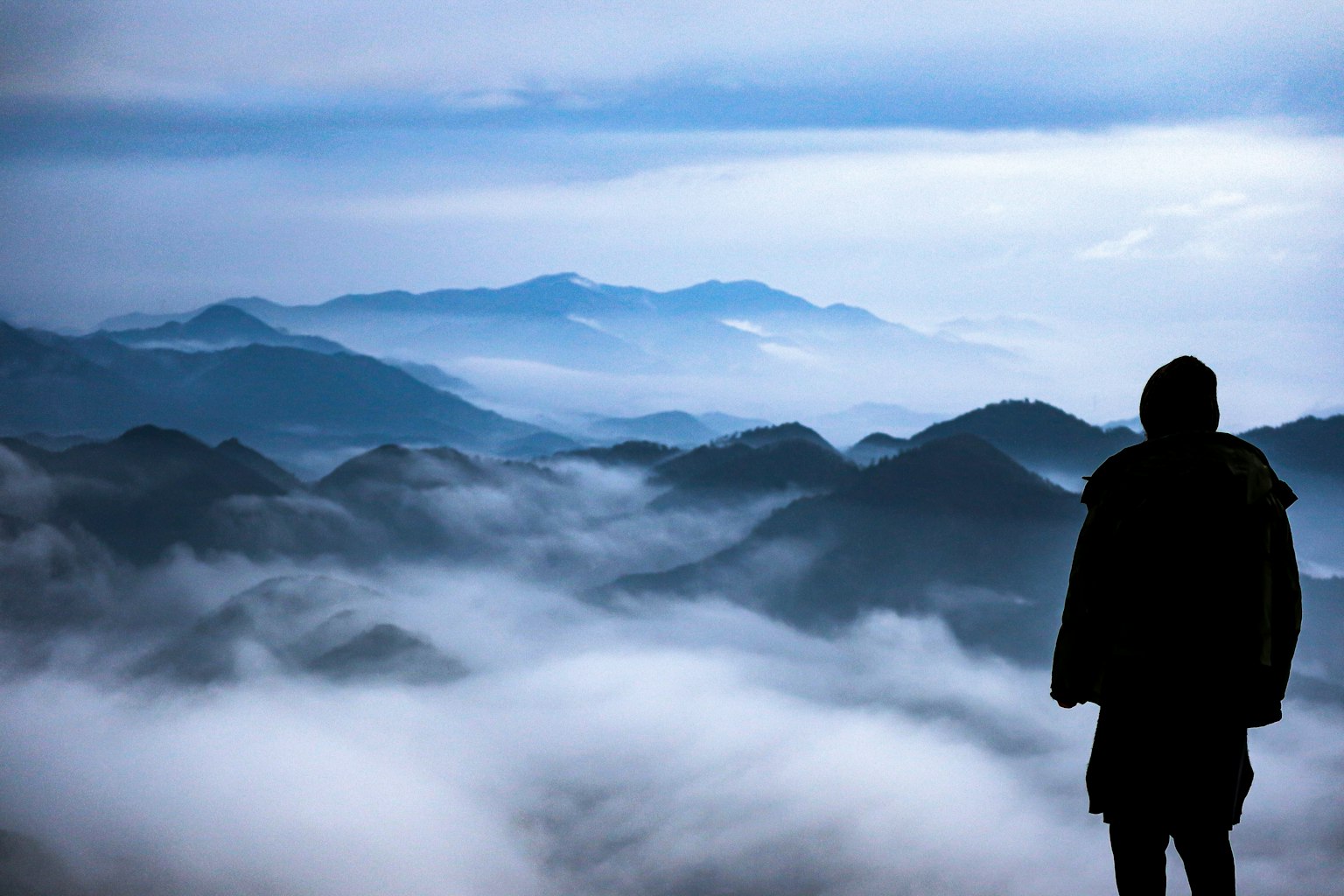 Siluet seseorang yang menatap gunung yang diselimuti kabut