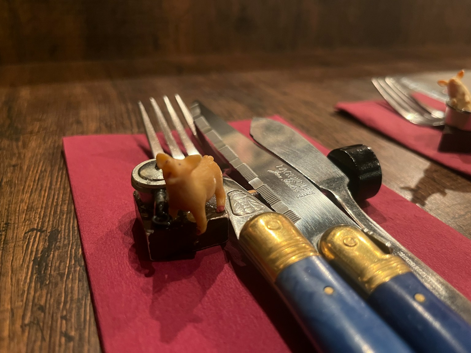 Une petite figurine d'animal brun placée sur un couteau et une fourchette dans une mise en place de table