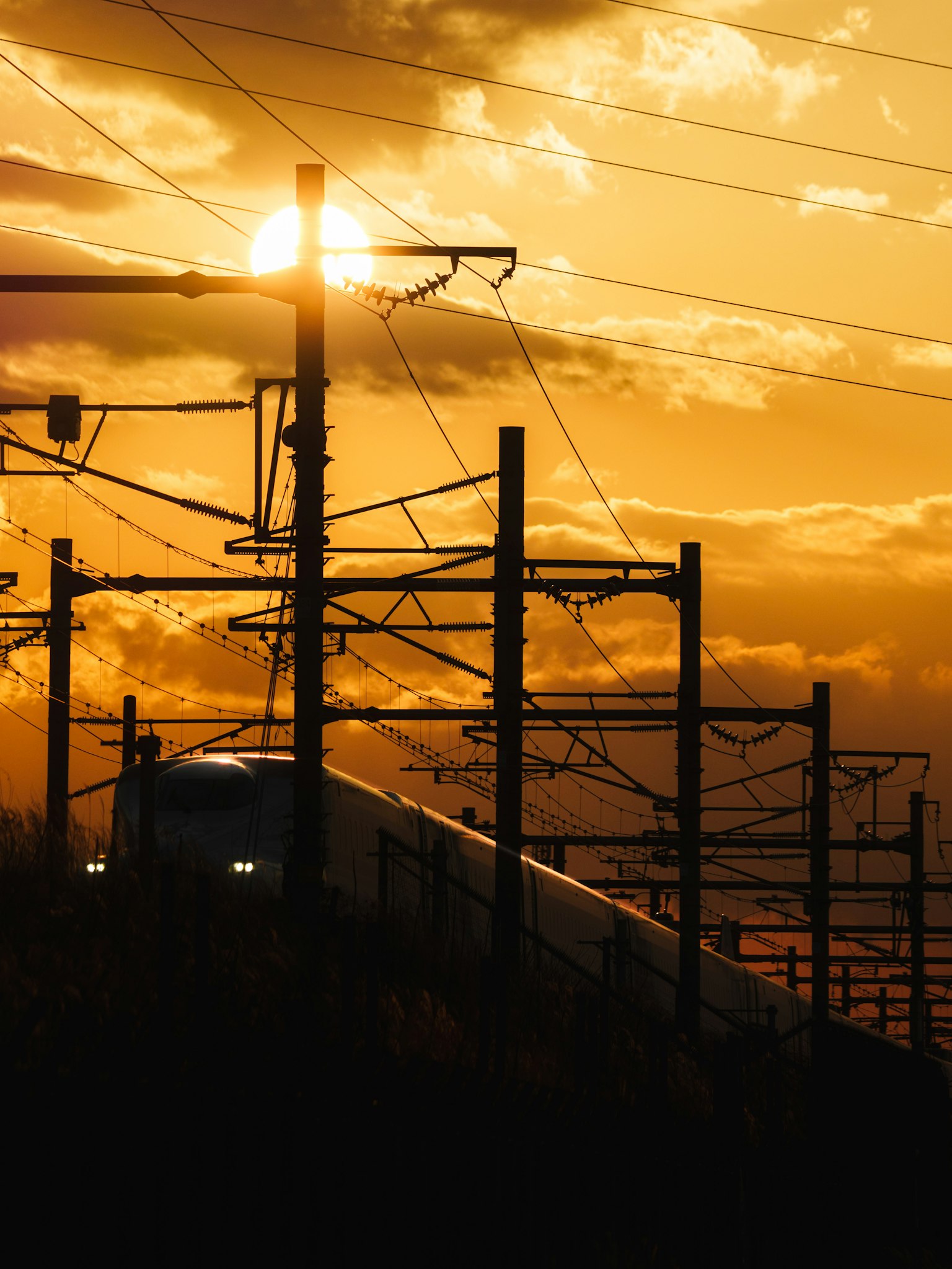 Silhouette di un treno e pali elettrici al tramonto