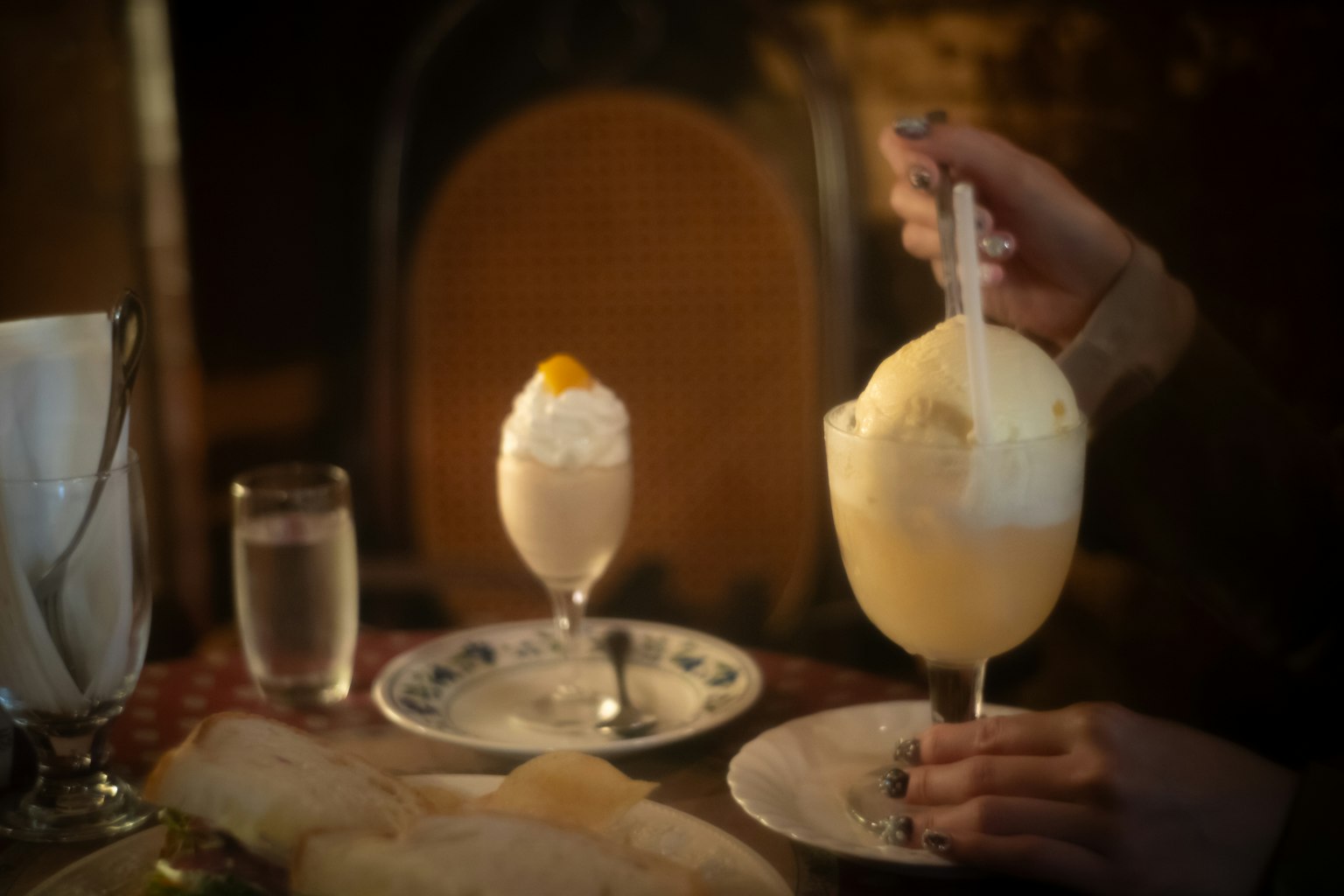 A person holding a spoon over a large ice cream dessert topped with whipped cream and a fruit garnish