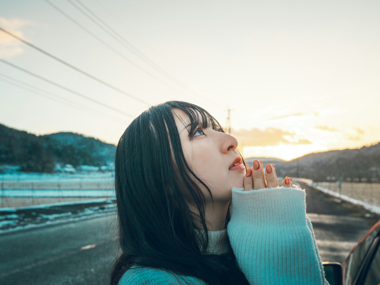 ผู้หญิงมองขึ้นไปที่ท้องฟ้าพนมมืออธิษฐานพระอาทิตย์ตกและภูเขาในพื้นหลัง