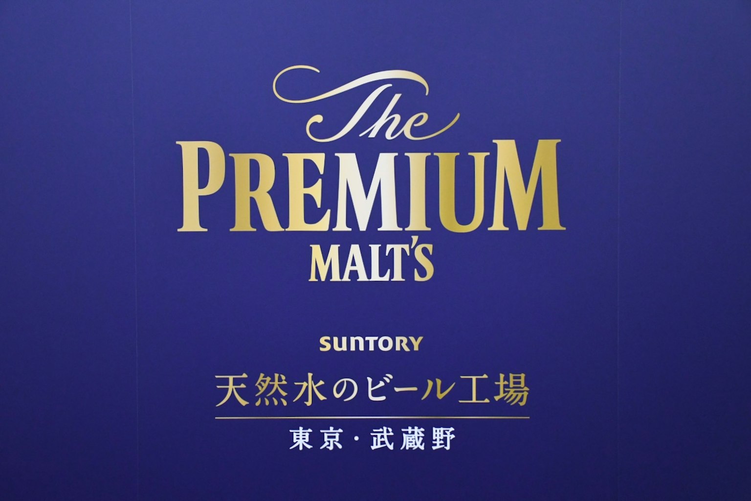 Logo-Design von Suntorys The Premium Malt's mit blauem Hintergrund und goldenen Buchstaben