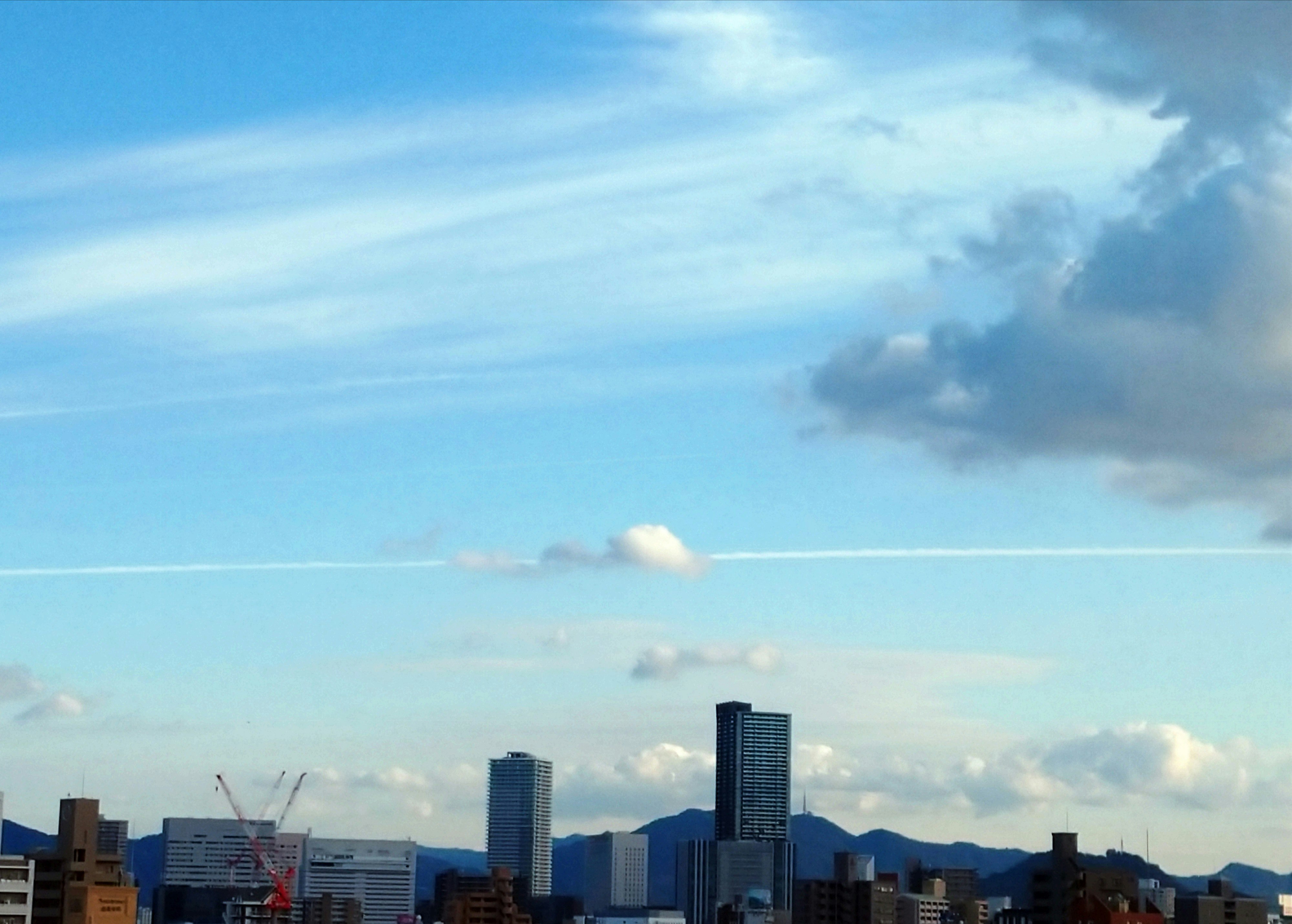 青空に広がる飛行機雲と雲のある都市のスカイライン