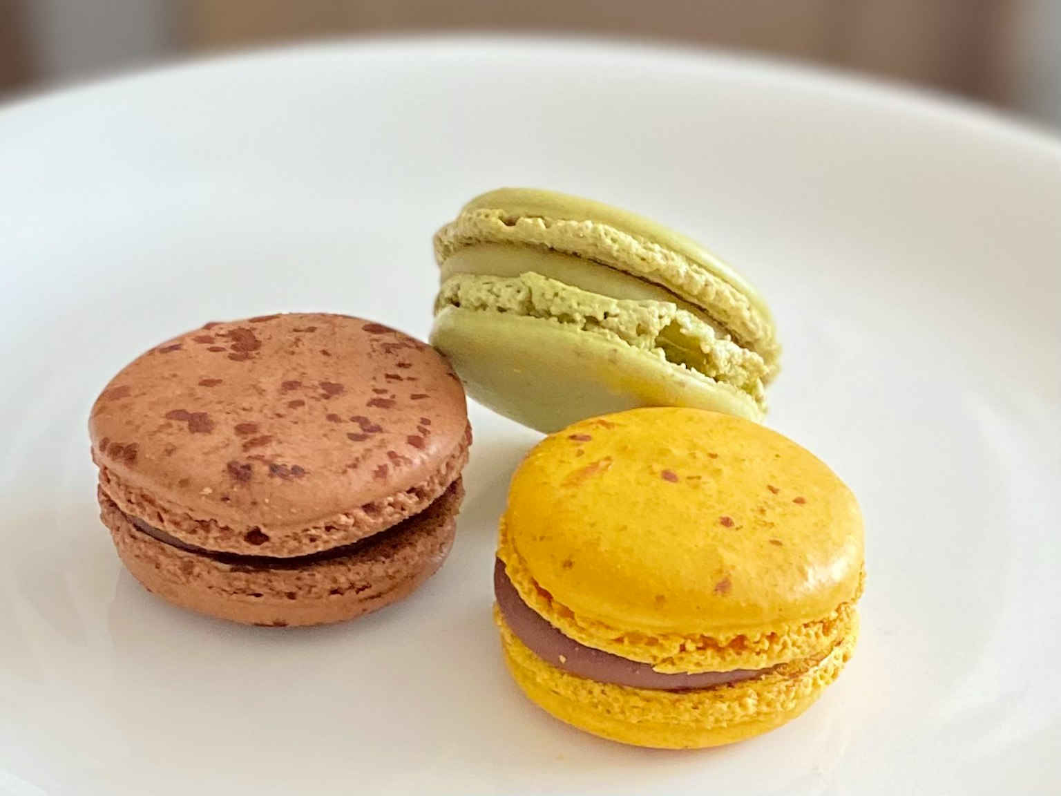 Three macarons on a white plate featuring brown, yellow, and green colors