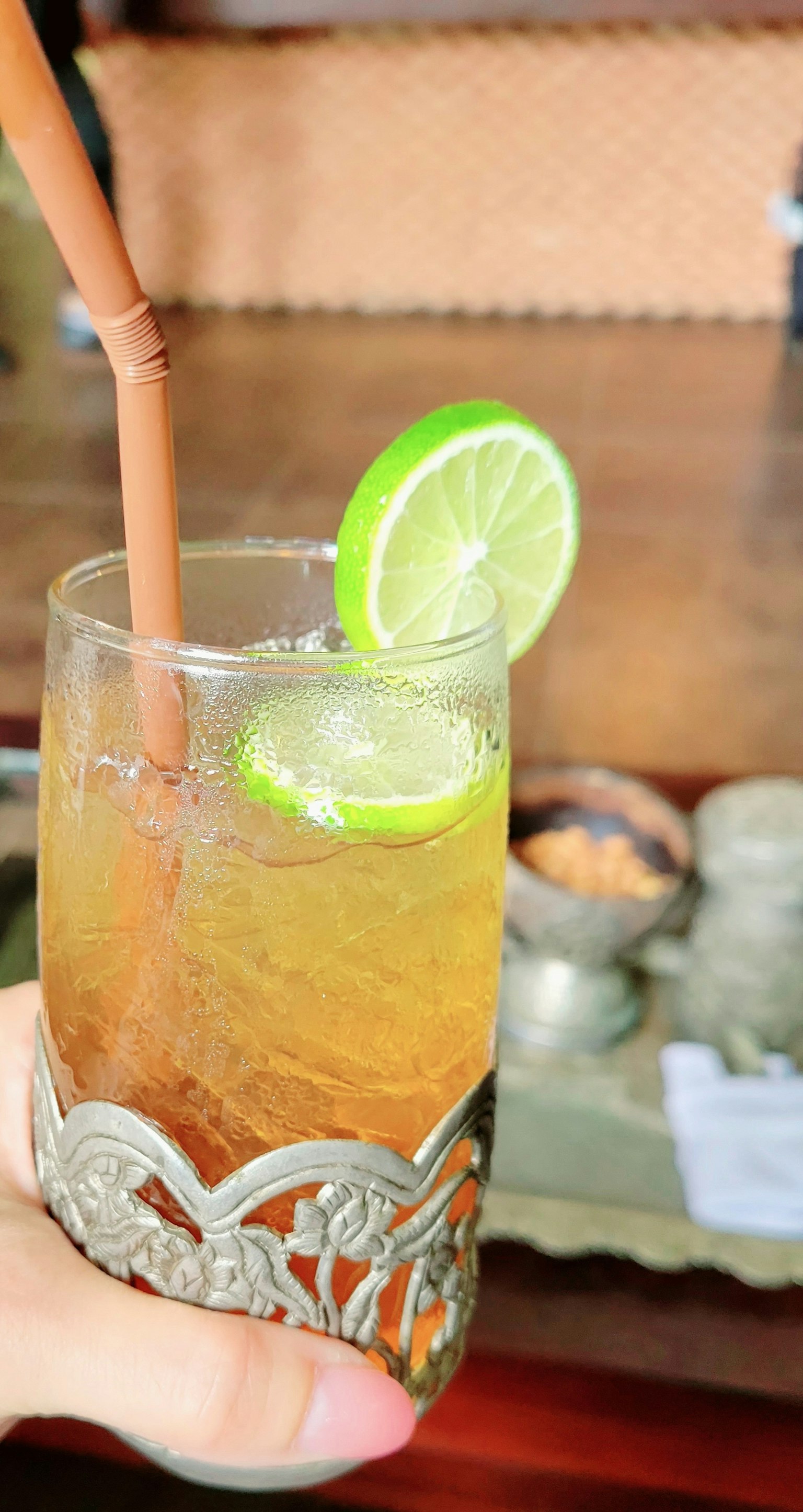 手中握着的装饰性玻璃杯，里面有饮料和一片青柠