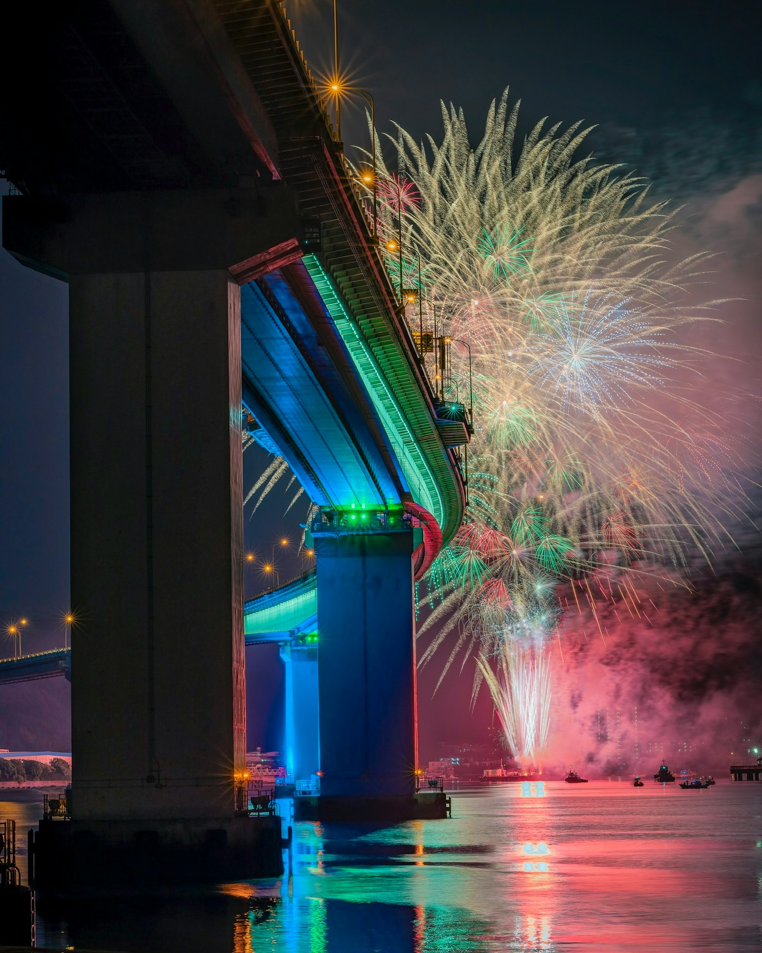 Espectáculo de fuegos artificiales bajo un puente de noche reflejos coloridos en el agua