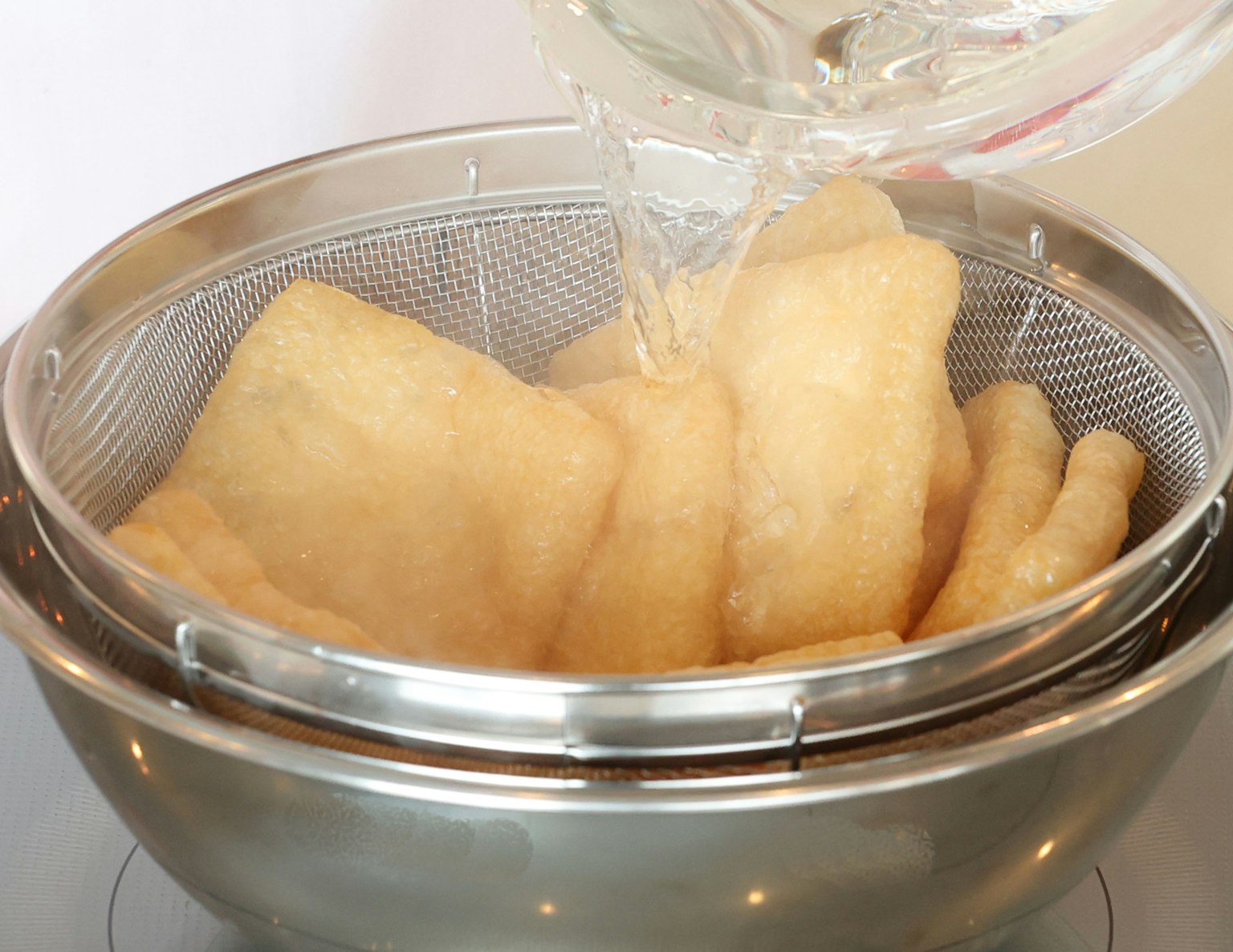 Versare acqua calda su cibo fritto in un colino in acciaio inox