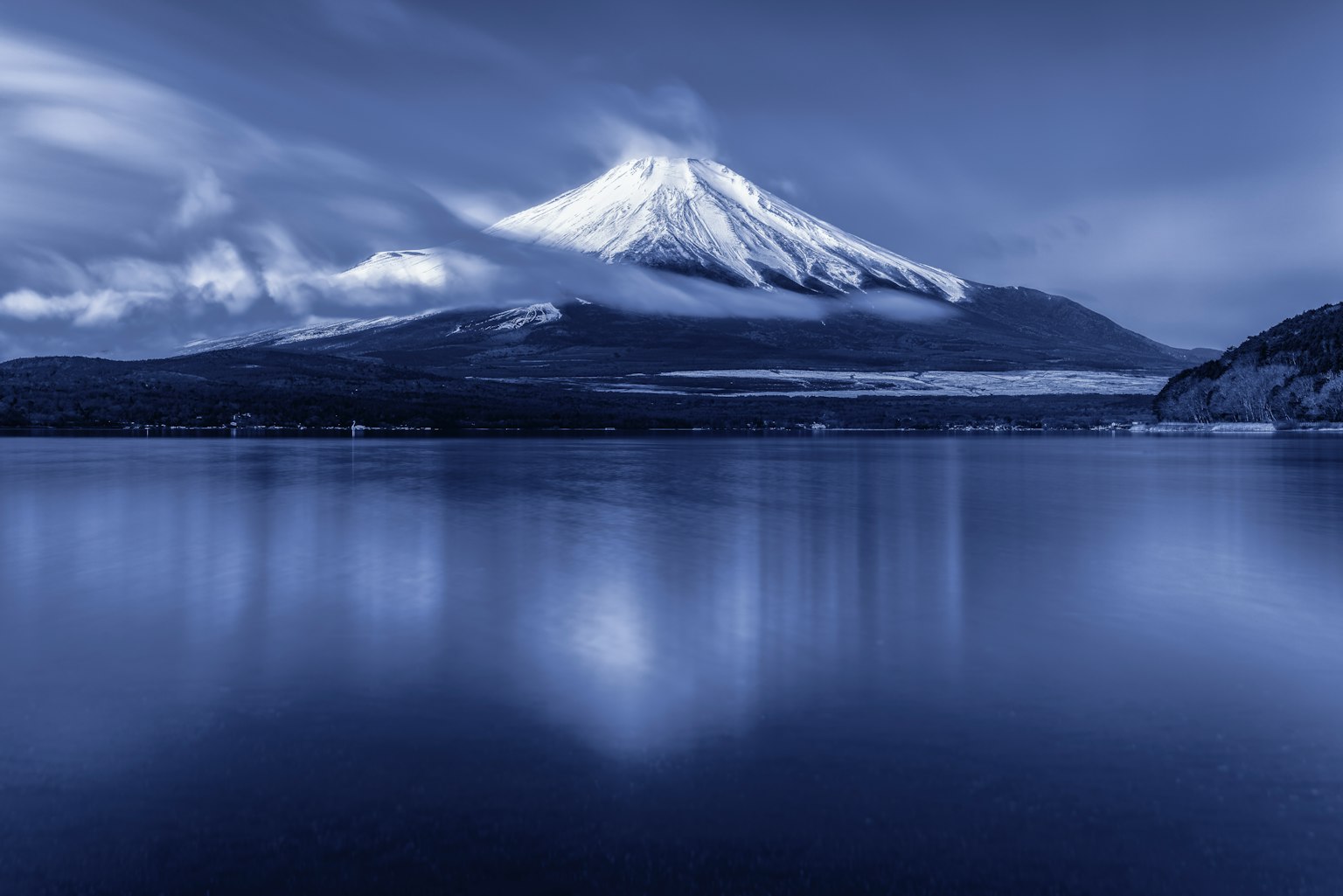 Mount Fuji reflected in a calm lake with a blue hue
