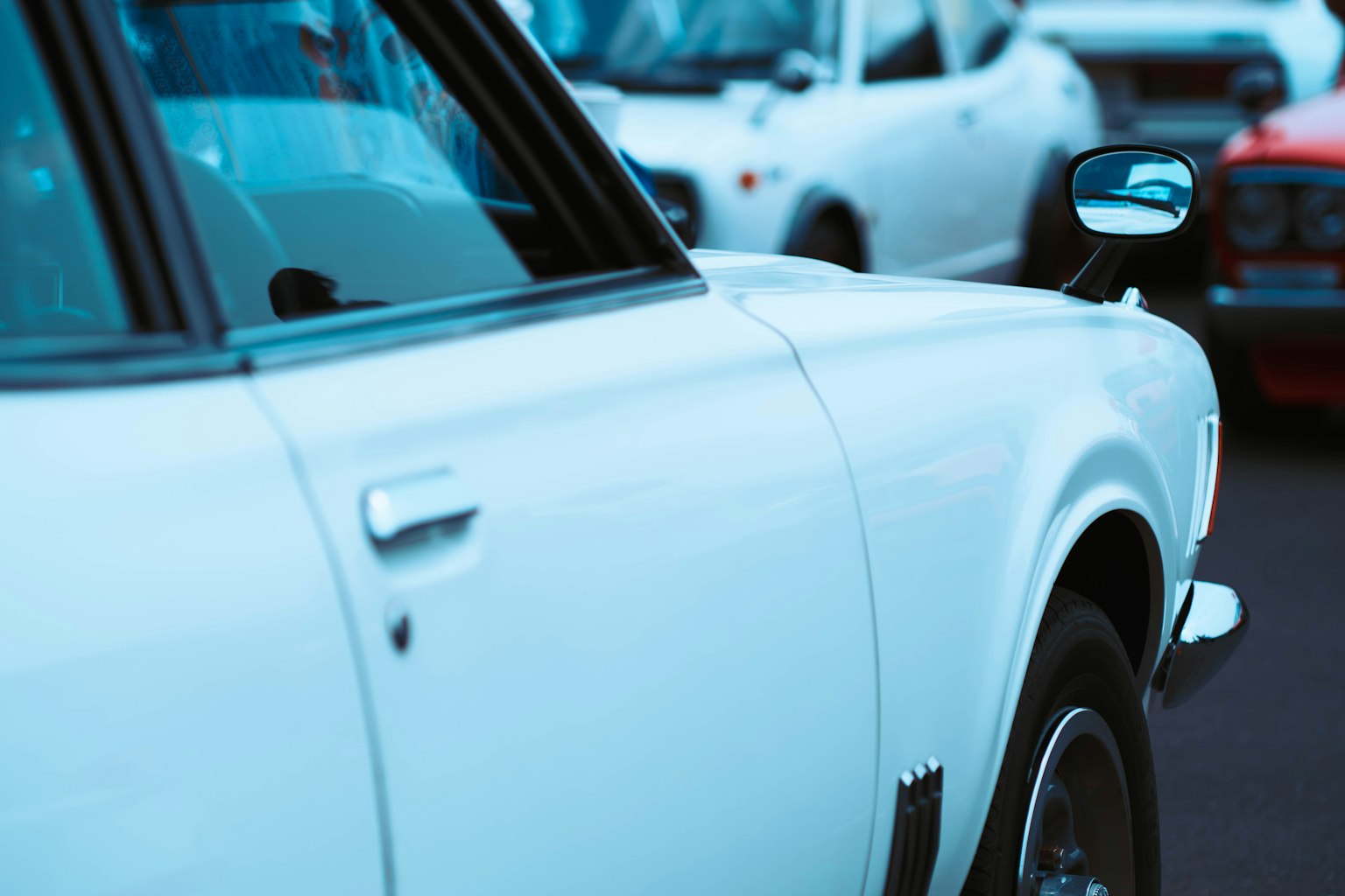 Góc nhìn bên hông của một chiếc xe cổ màu trắng với các xe khác ở phía sau