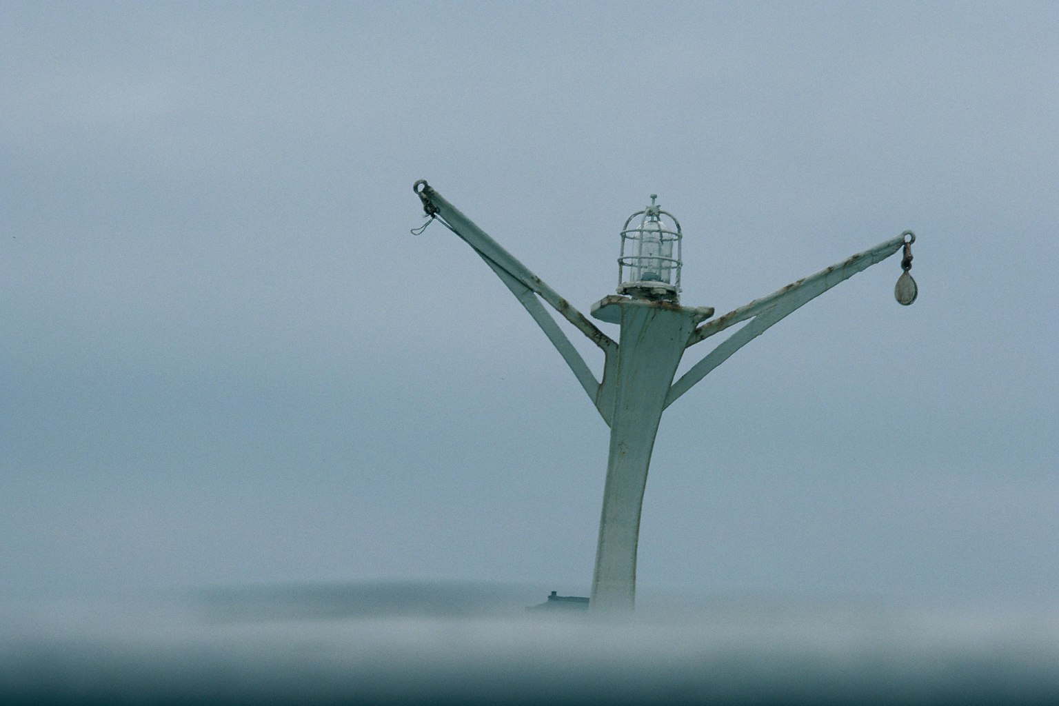 A lighthouse-like structure stands above the ocean shrouded in mist
