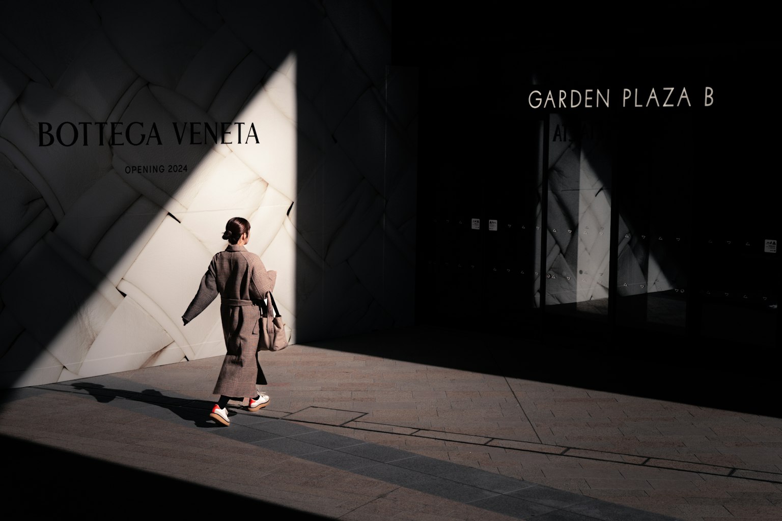 Una donna che cammina su una strada poco illuminata con insegna Bottega Veneta