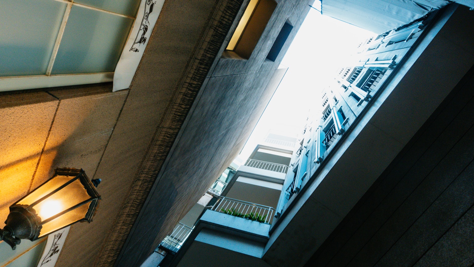 Regard vers le haut dans un passage étroit avec une lumière vive et un vieux lampadaire contrastant avec des bâtiments modernes