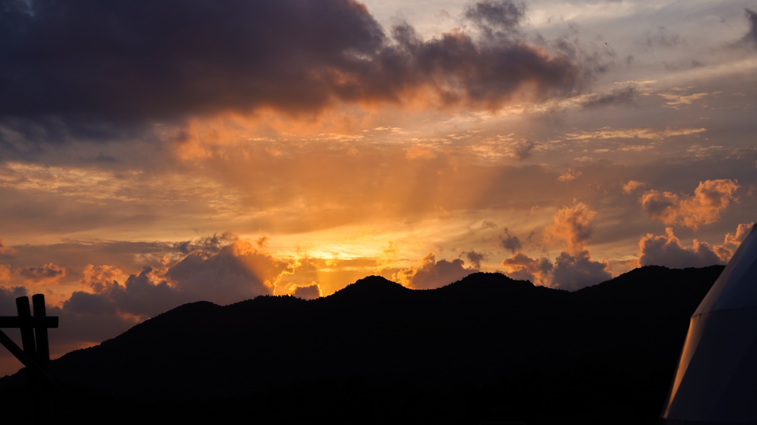 Matahari terbenam di balik gunung dengan awan oranye yang menyebar di langit