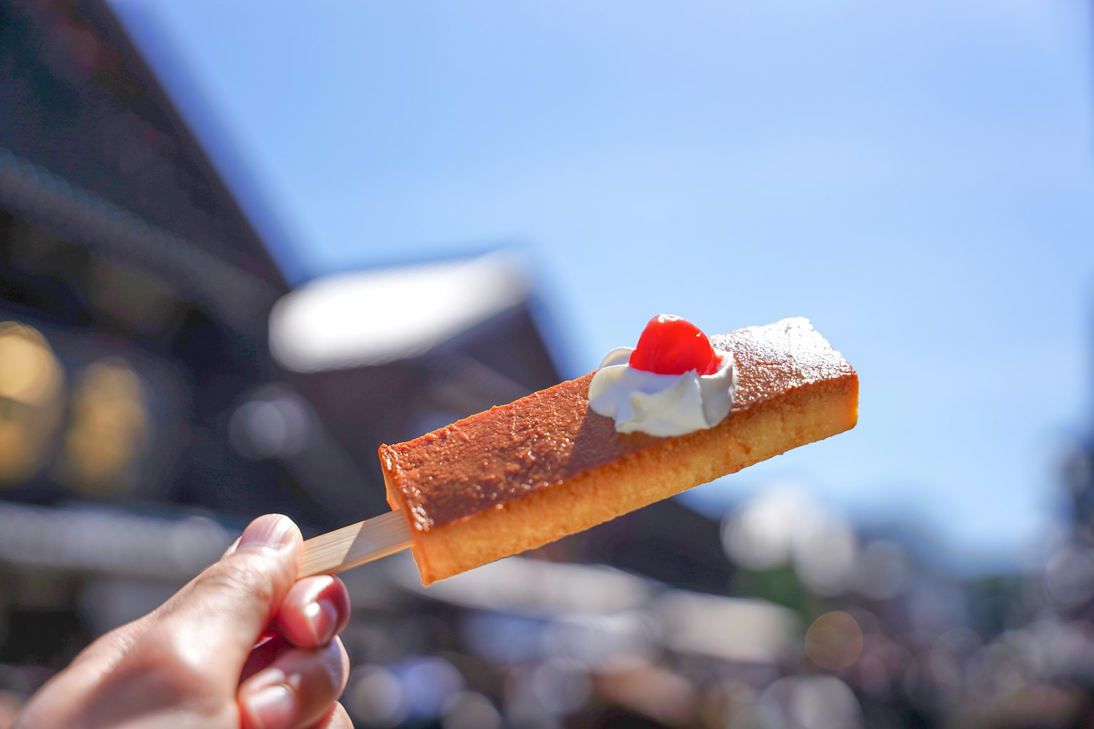 มือหนึ่งถือไอศกรีมที่มีครีมและเชอร์รี่ประดับอยู่ใต้ท้องฟ้าสีฟ้า