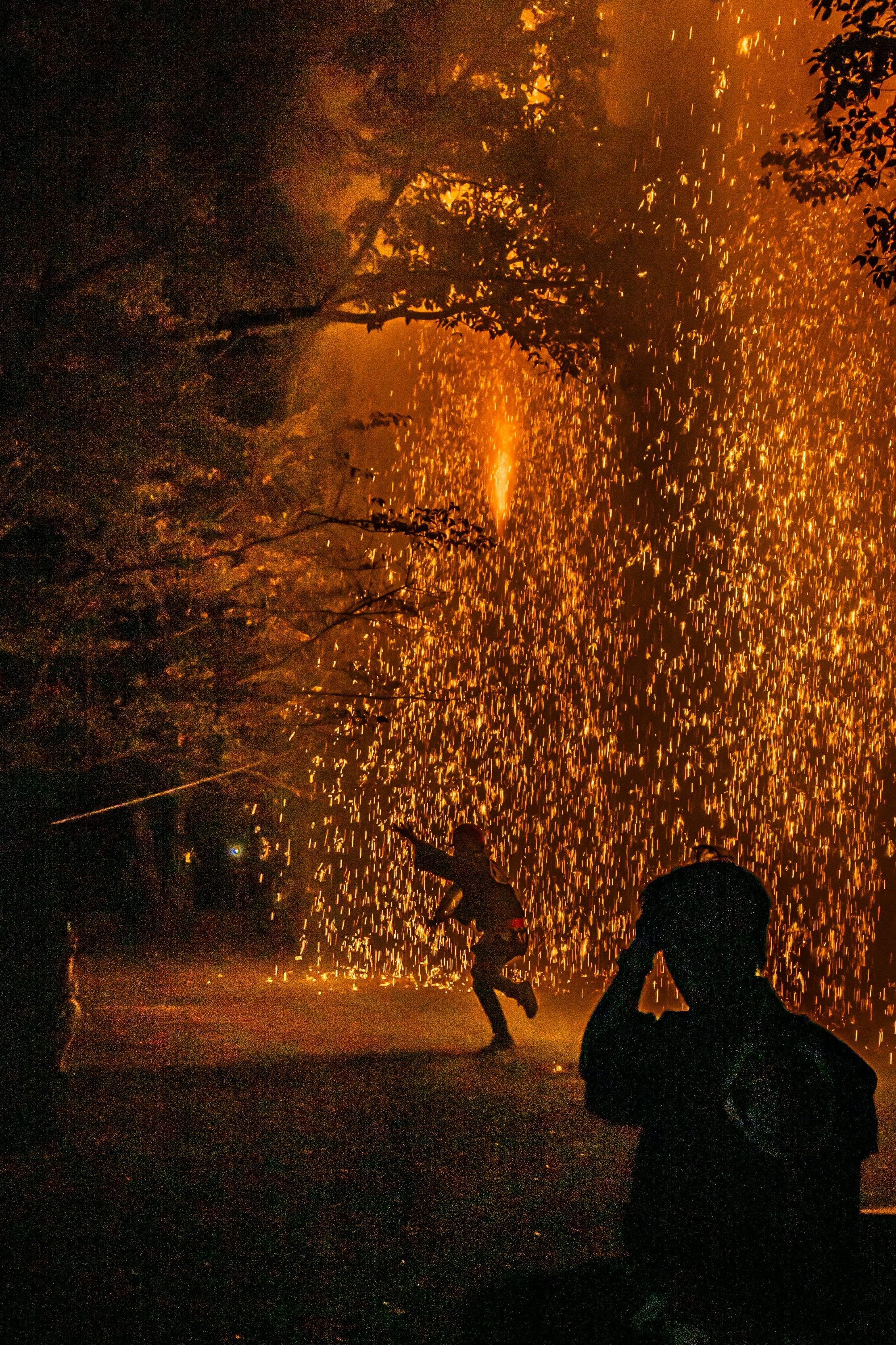 silhouette of a person in a park with fireworks sparks at dusk