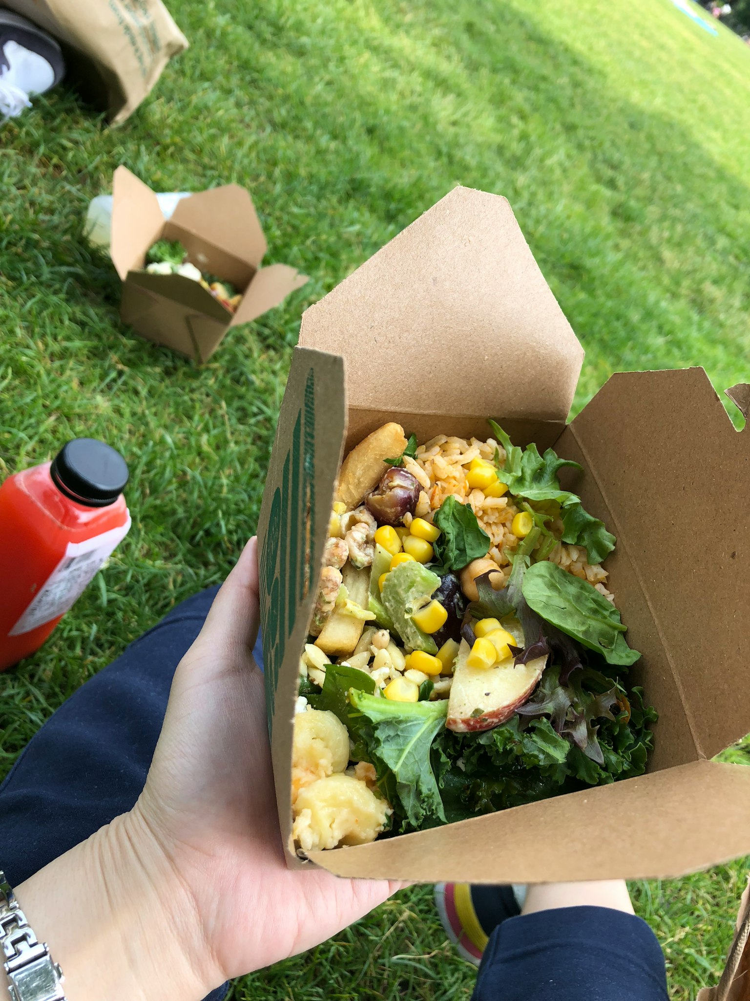 Main tenant un bol de salade avec des légumes verts et du maïs sur l'herbe avec des boîtes de nourriture en arrière-plan