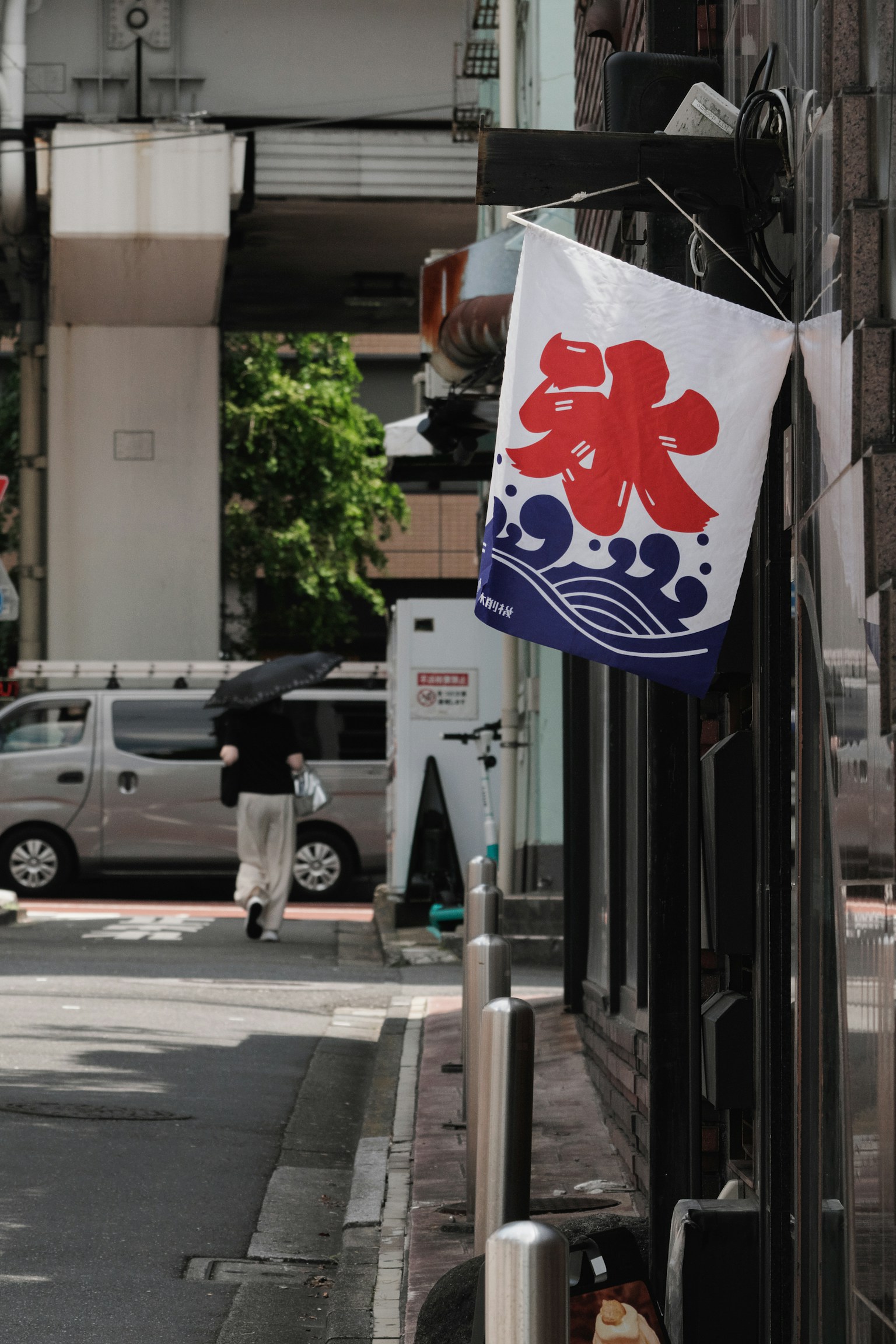 Pemandangan jalan dengan papan nama toko yang menampilkan desain gelombang biru dan kanji merah untuk es