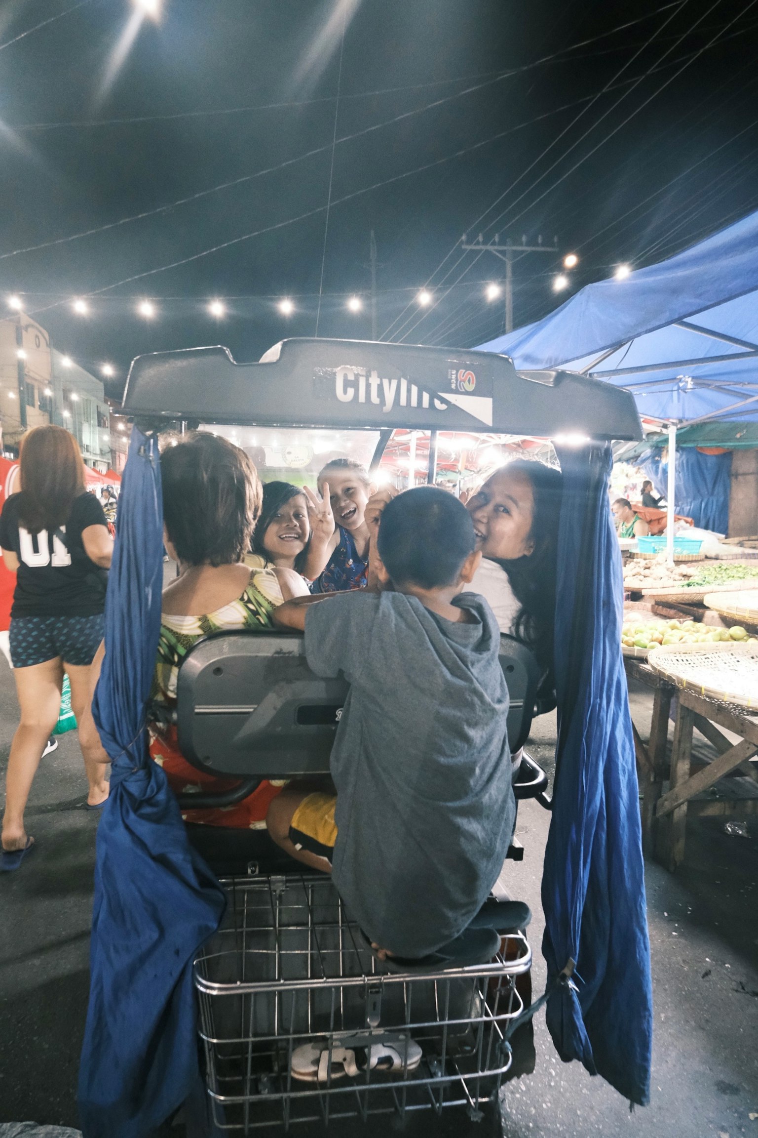夜市で買い物カートに座る子供たちと周囲の人々