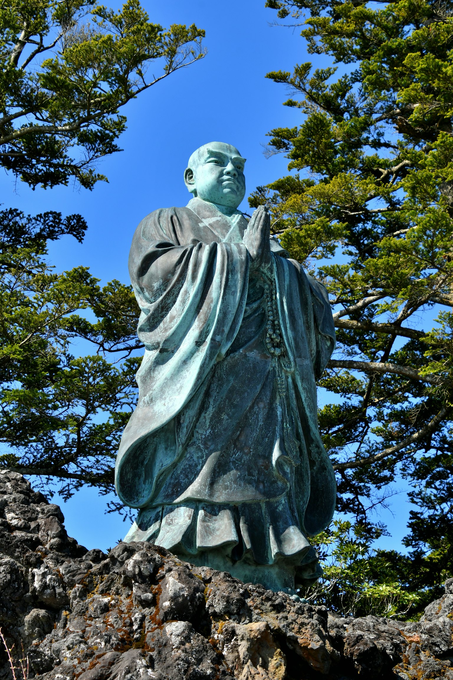A bronze statue of a monk standing amidst lush greenery