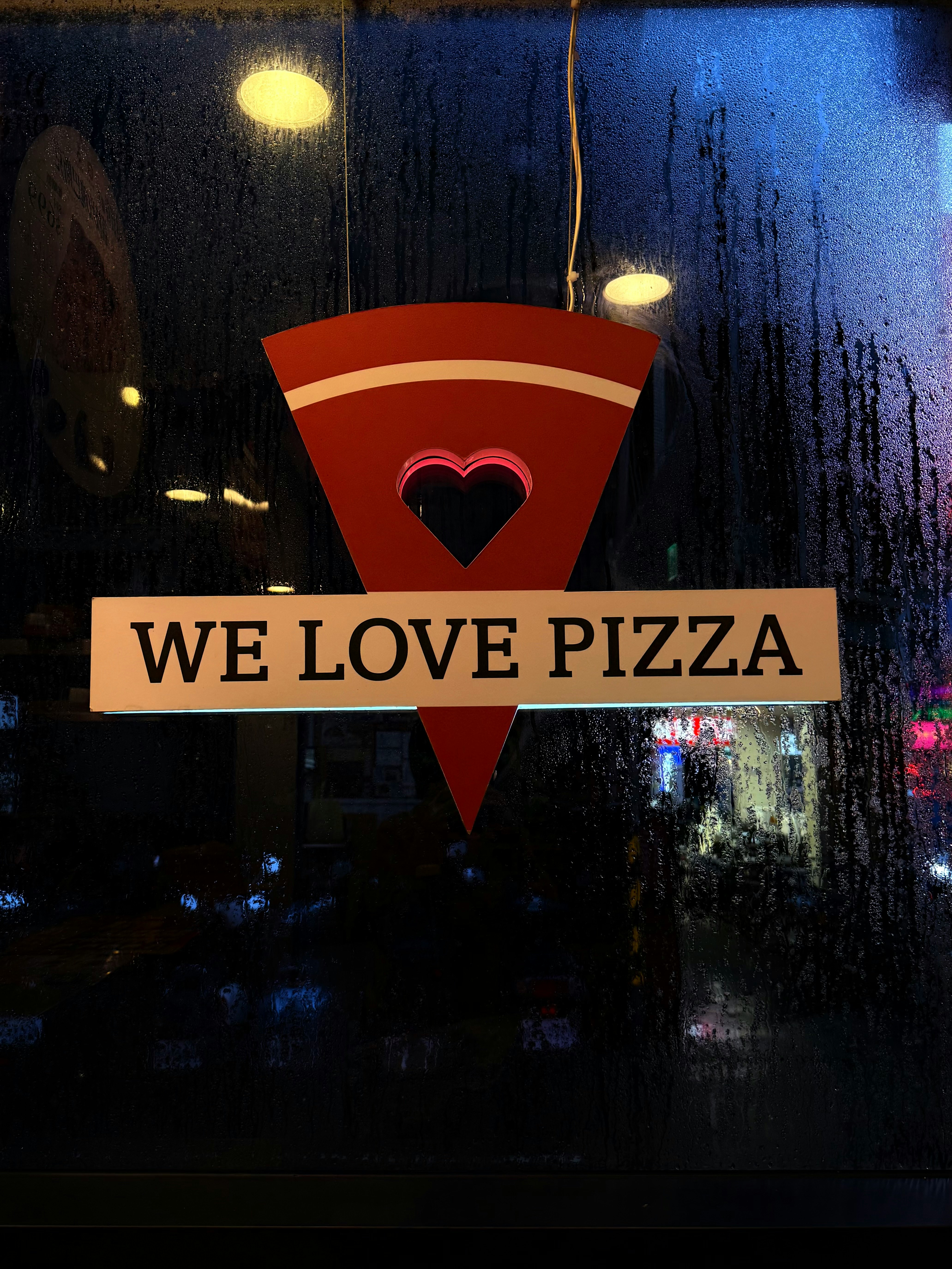 雨の夜の窓に映る「WE LOVE PIZZA」看板