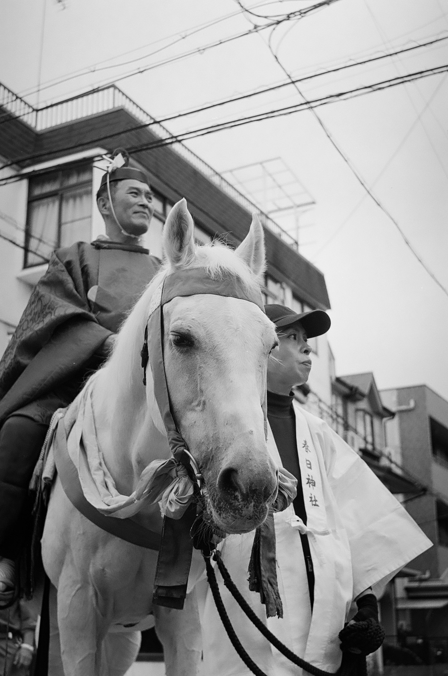 黑白照片中一名騎在白馬上的男子和旁邊站著的男子城市背景可見