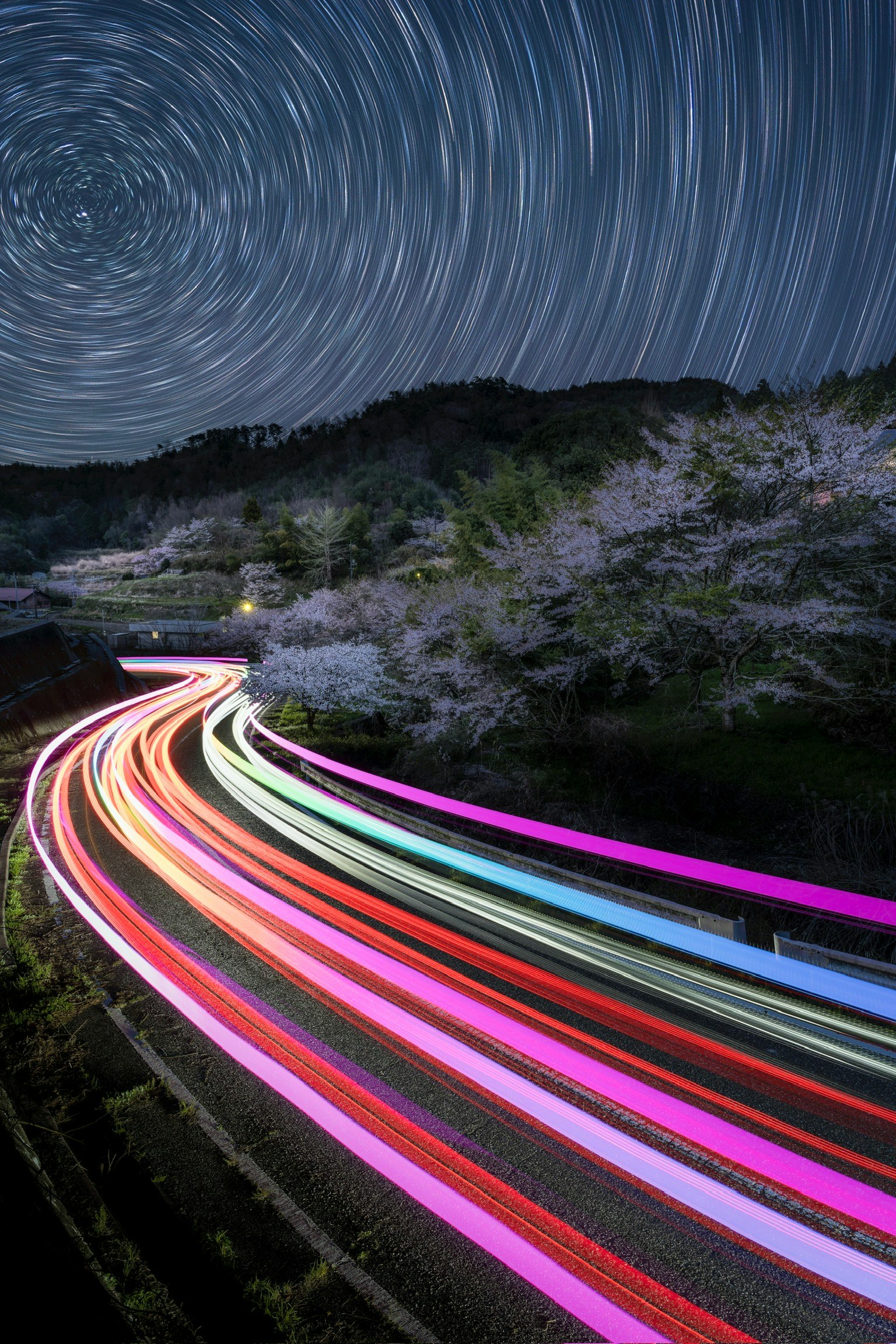 Une route sinueuse illuminée par des traînées de lumière colorées sous un ciel étoilé