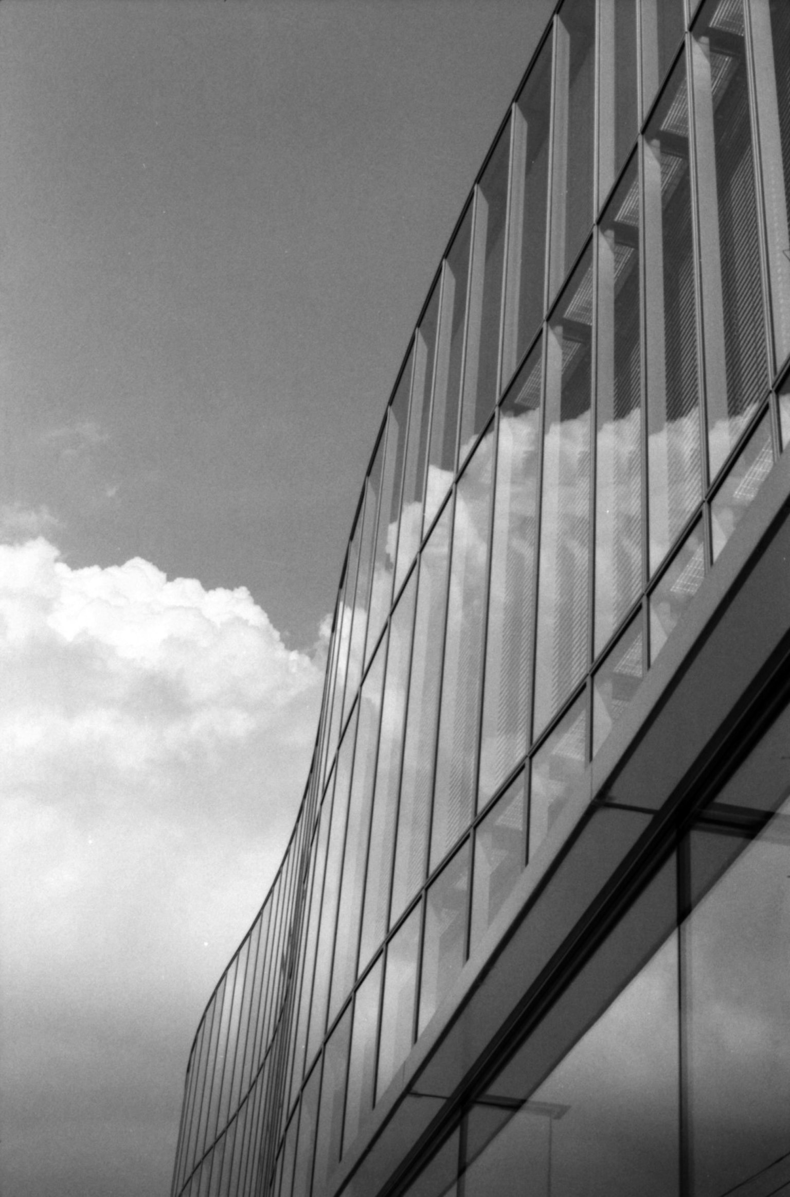 Façade en verre courbée d'une architecture moderne reflétant des nuages