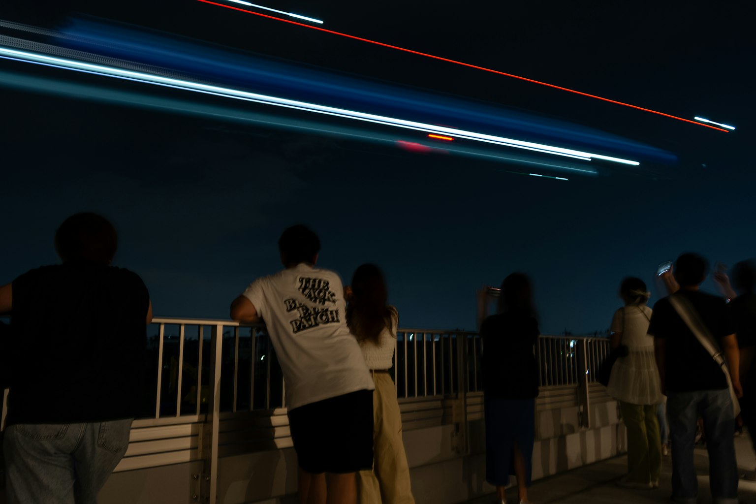 夜空を見上げる人々と飛行機の光跡