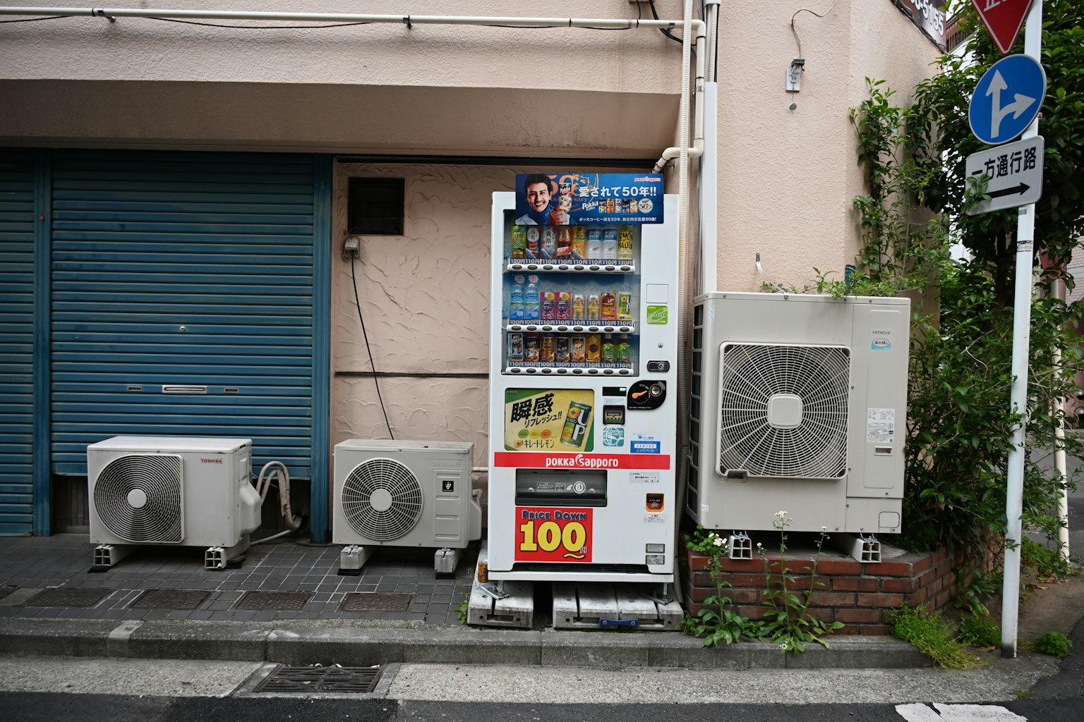 Distributore automatico all'angolo della strada con unità di climatizzazione serranda blu e piante verdi sullo sfondo