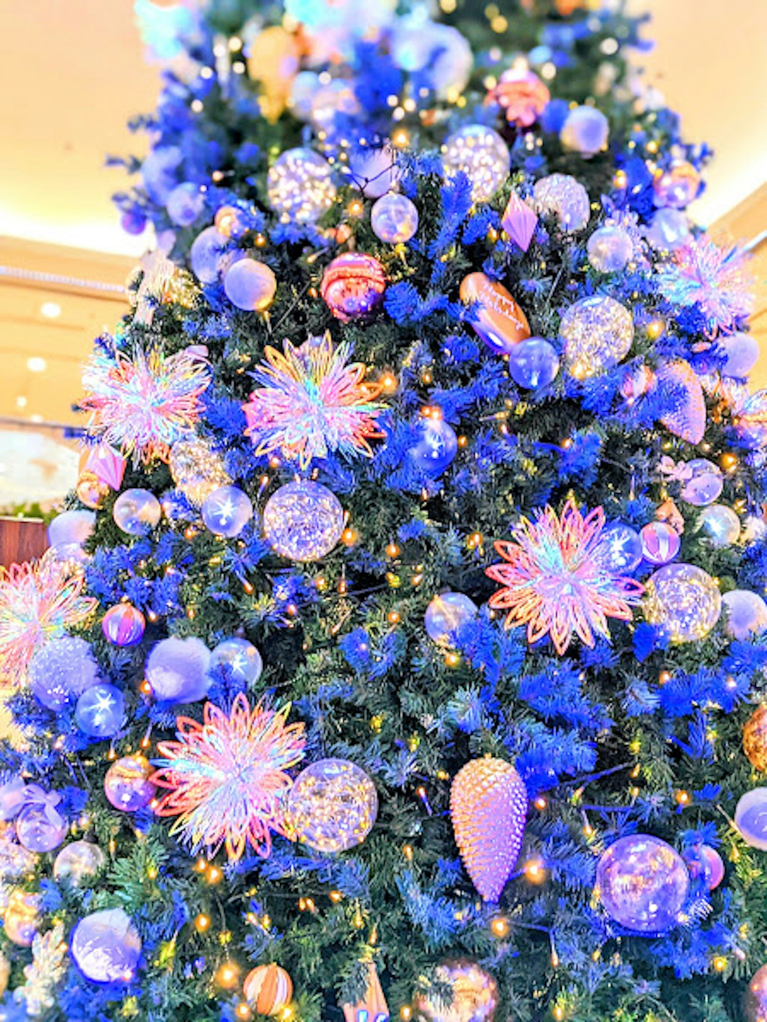 A Christmas tree adorned with blue decorations featuring colorful ornaments and sparkling lights