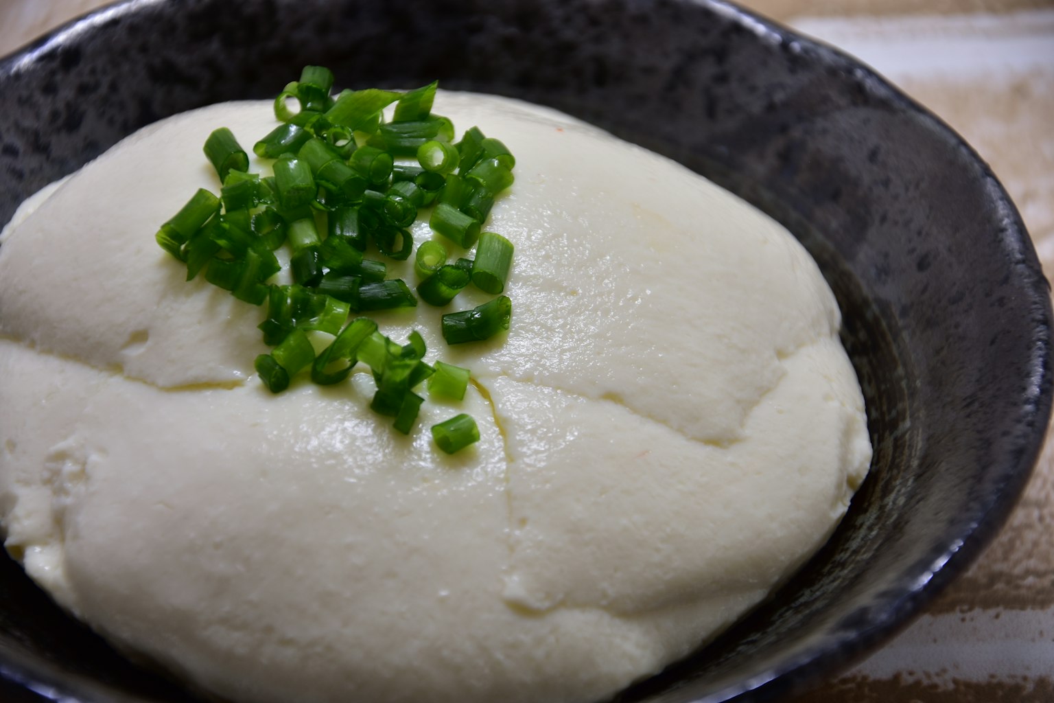 Eine Schüssel mit weichem Tofu, garniert mit gehackten Frühlingszwiebeln
