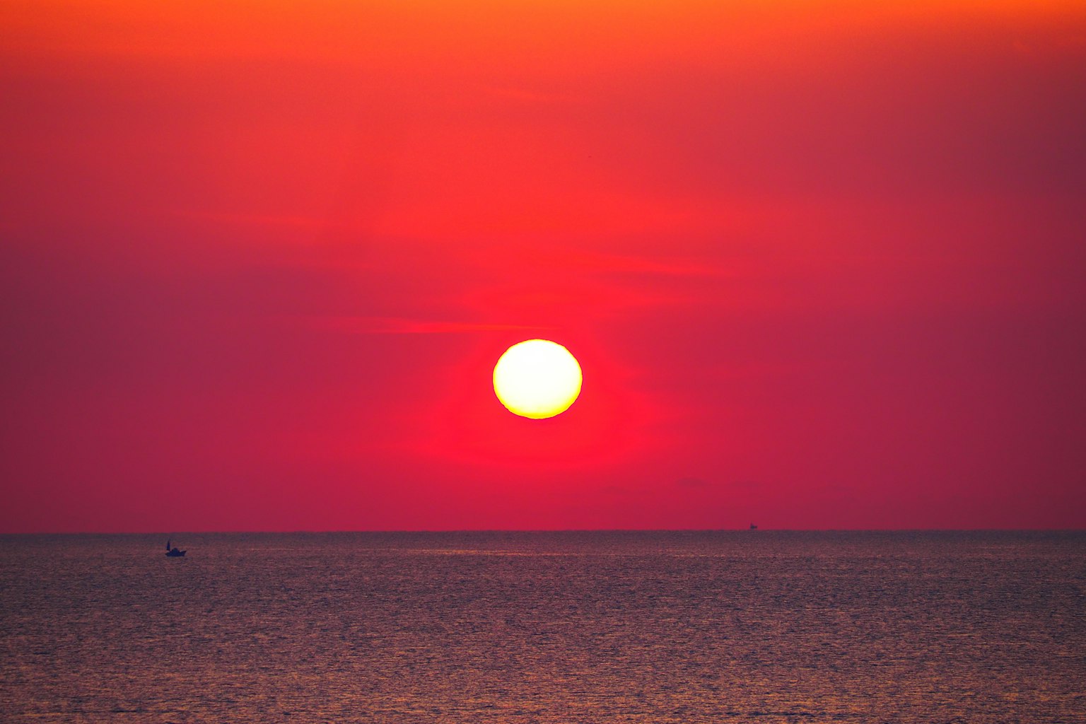 Sebuah matahari terbenam yang indah di atas laut dengan matahari besar dan langit merah cerah