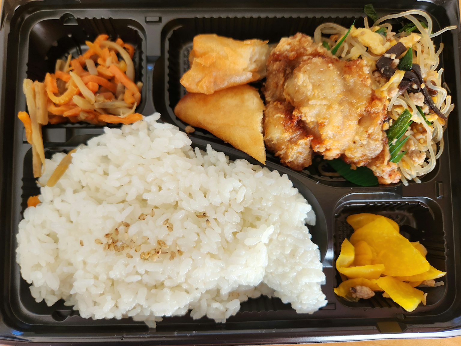 一个便当盒，里面有白米饭，炸鸡，粉丝沙拉，炸饺子和蔬菜配菜