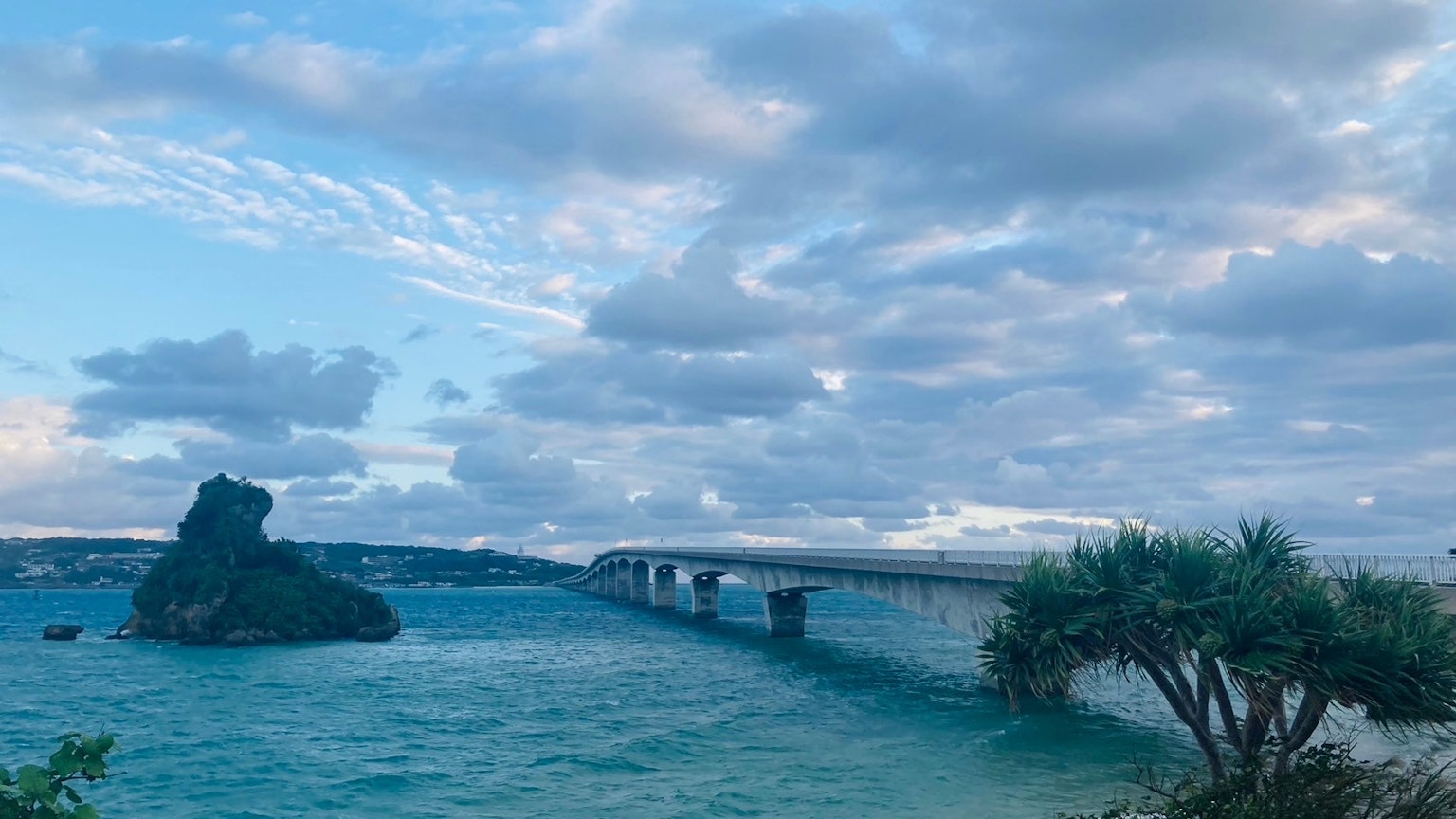 Eine malerische Aussicht auf eine Brücke über blaues Wasser mit einem Felsen und Wolken am Himmel