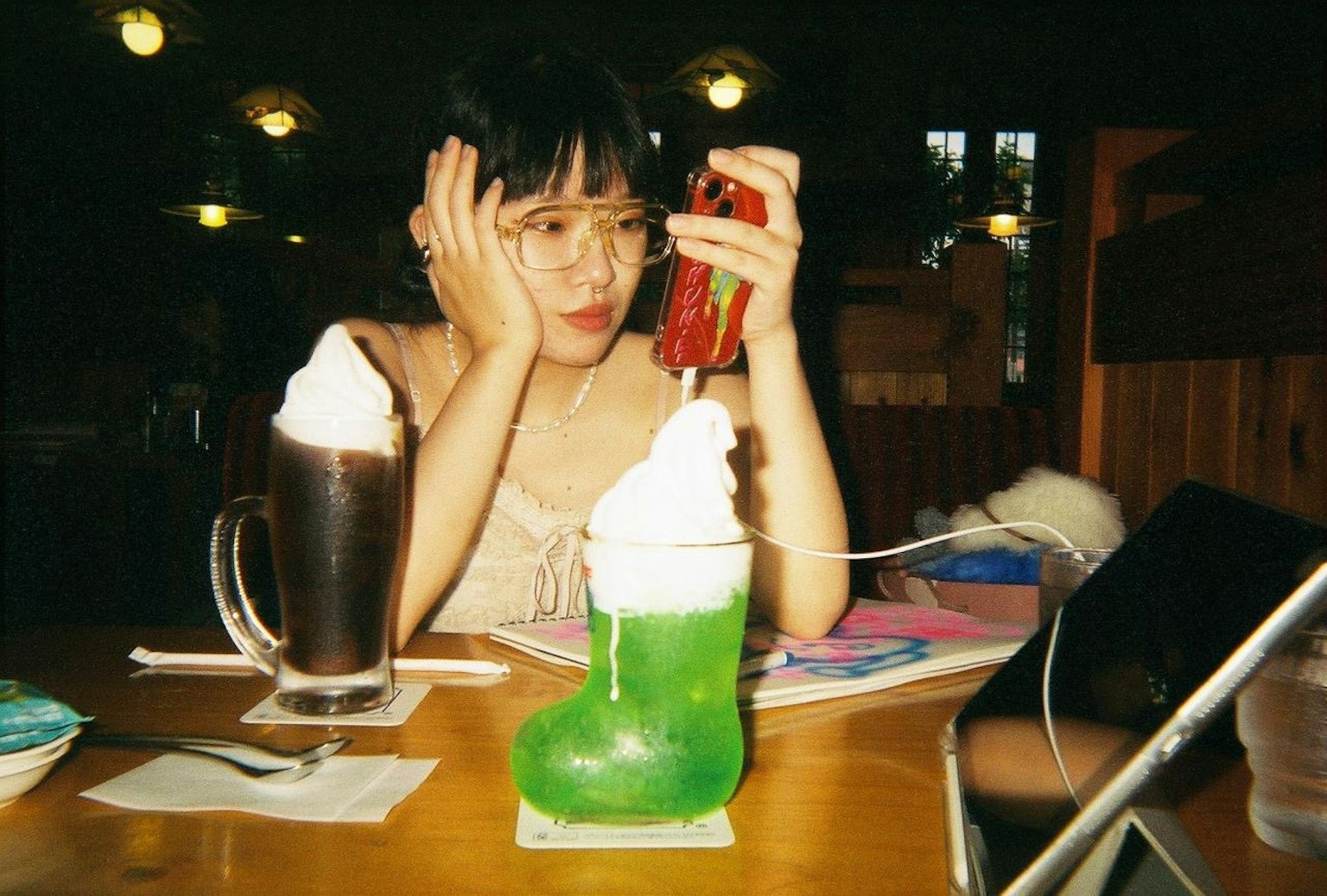 Seorang wanita di kafe menutupi wajahnya dengan satu tangan sambil memegang telepon di tangan lainnya