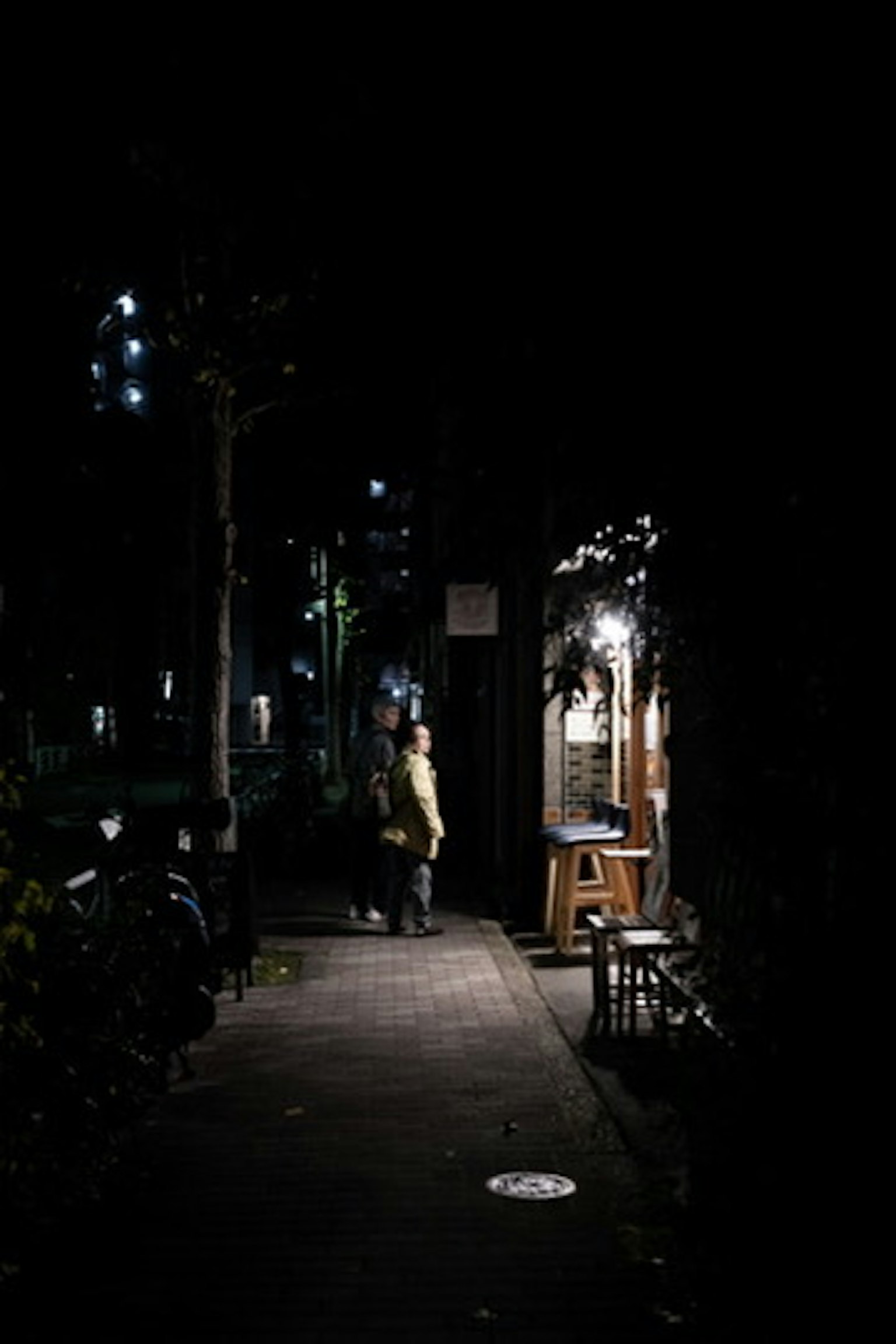 Una figura de pie en una calle oscura con el exterior de un café iluminado