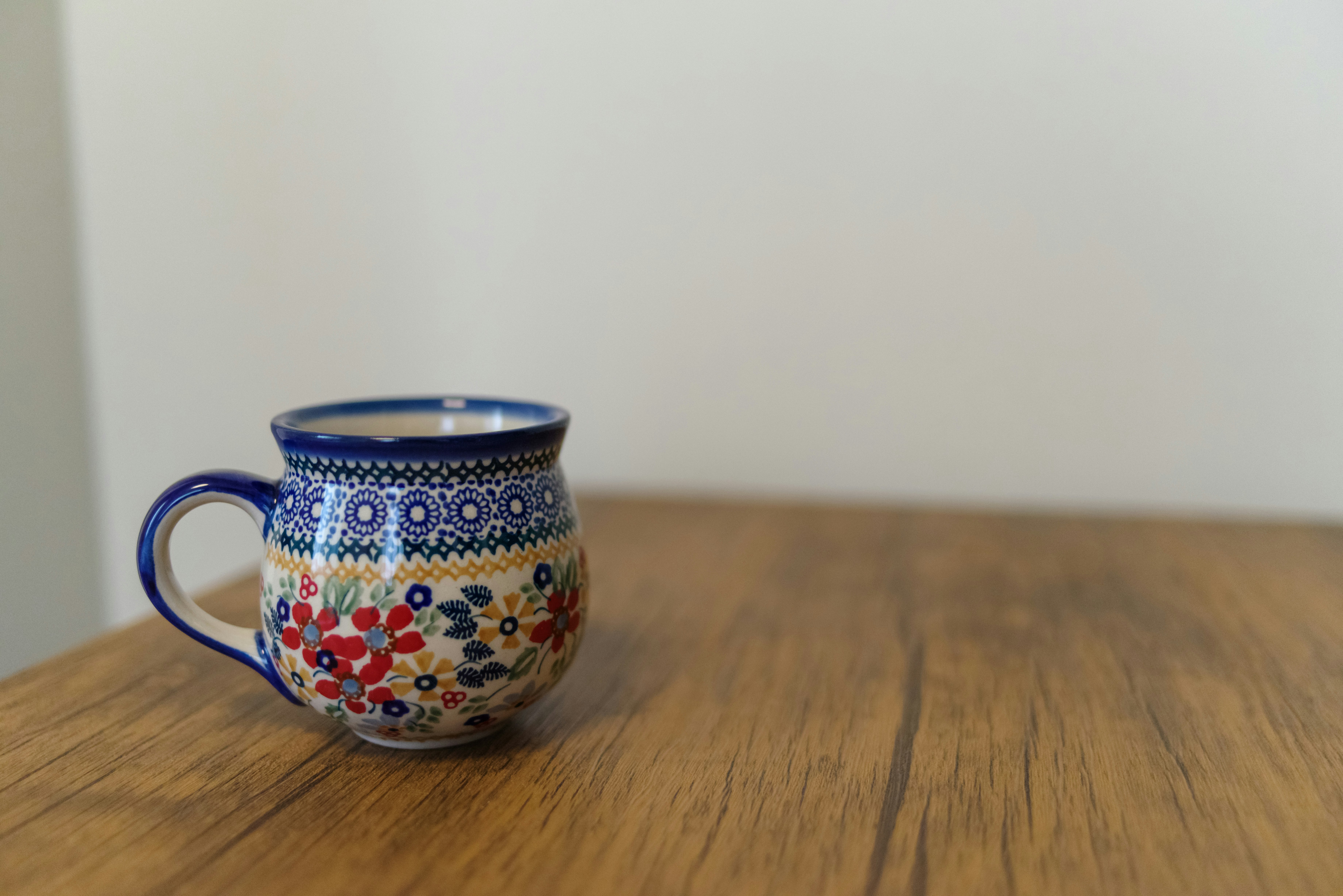 A colorful ceramic mug with blue rim and floral decorations placed on a wooden table