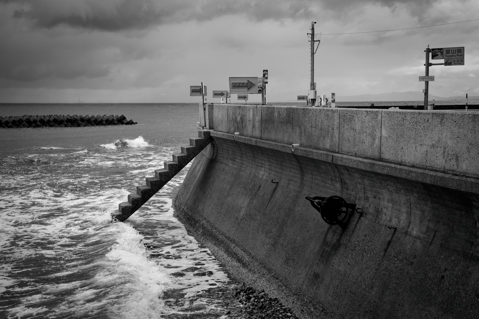 Monochrome Ansicht einer Betonmauer am Meer mit Wellen und bewölktem Himmel