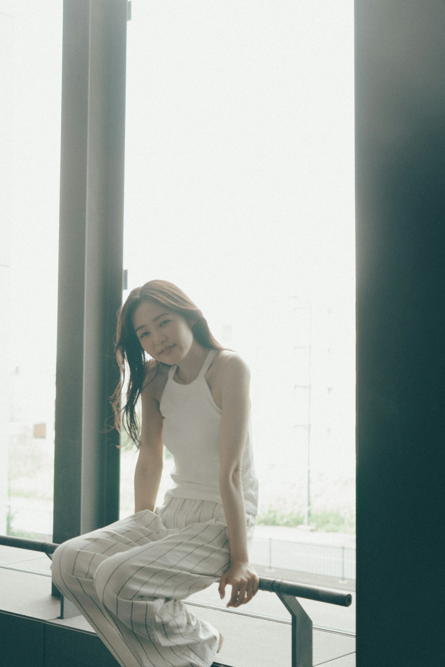 窗邊坐著的女性，面帶柔和微笑，身穿白色服裝