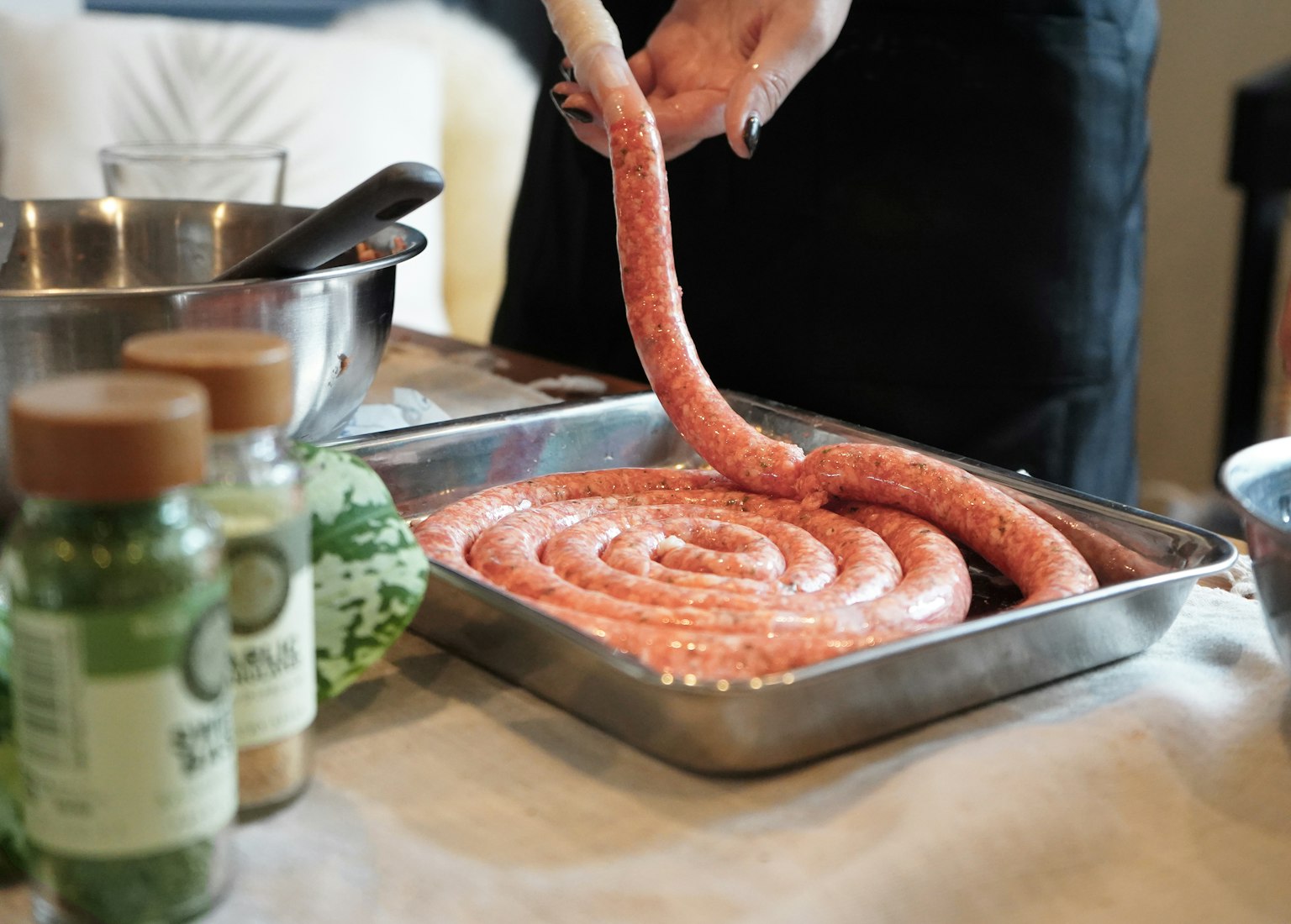 Une personne façonnant une saucisse à la main avec des ustensiles de cuisine et des bocaux d'épices visibles