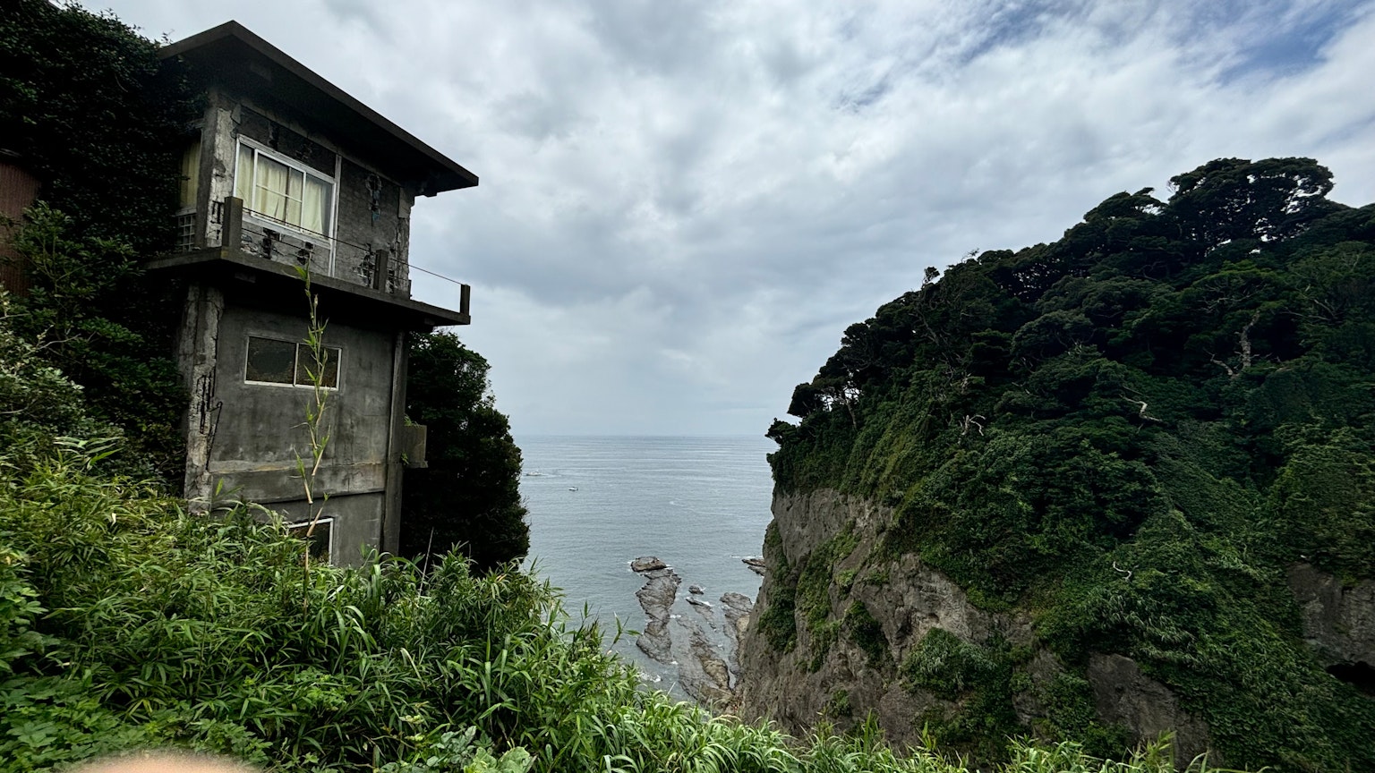 Abandoned building overlooking the sea with lush greenery on cliffs