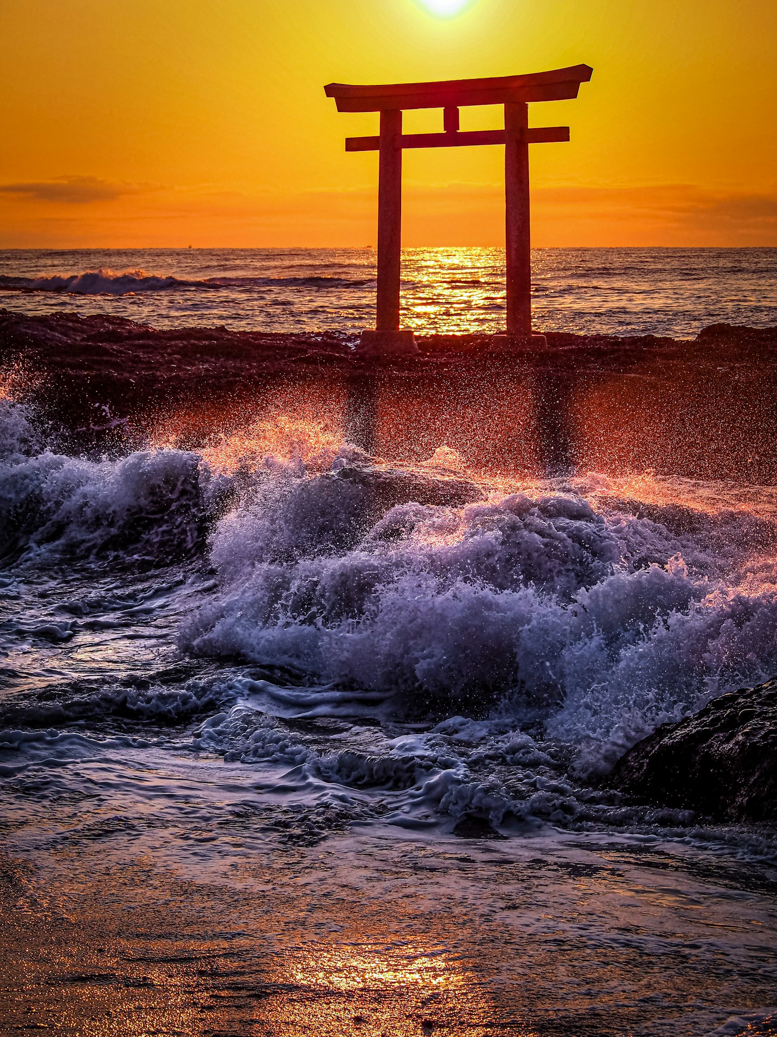 Torii gate silhouette against a vibrant sunset with crashing waves