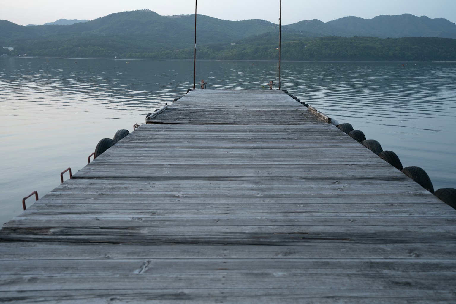 Ein Holzsteg, der in einen ruhigen See mit Bergen im Hintergrund führt