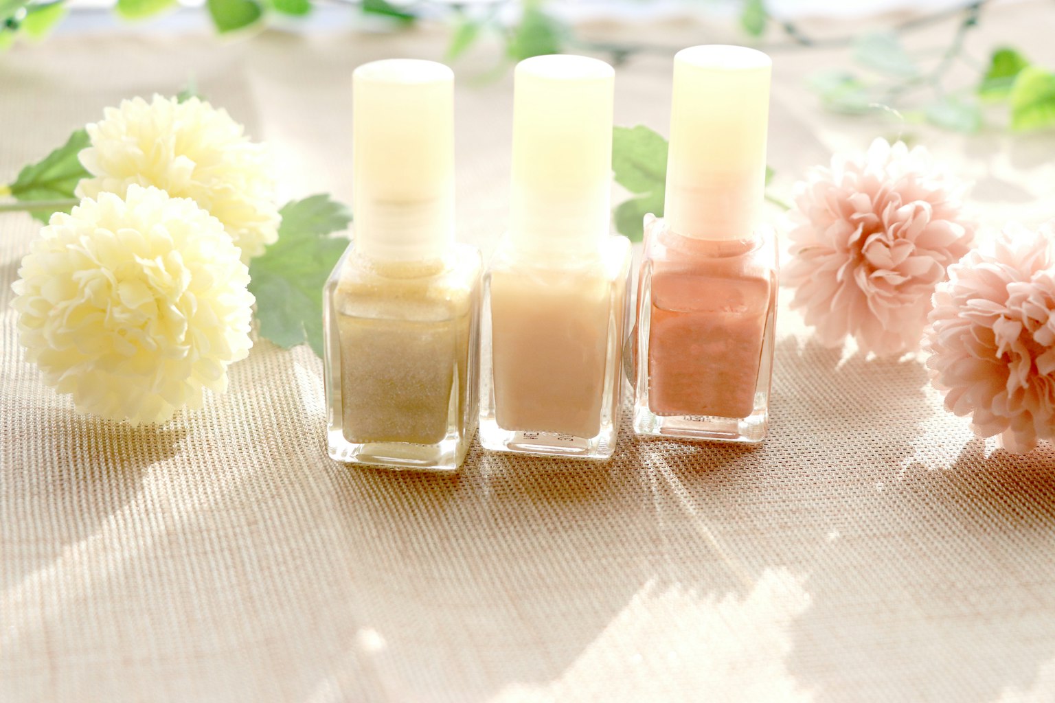 Pastellfarbene Nagellackflaschen angeordnet mit Blumen und Blättern in einer schönen Anordnung