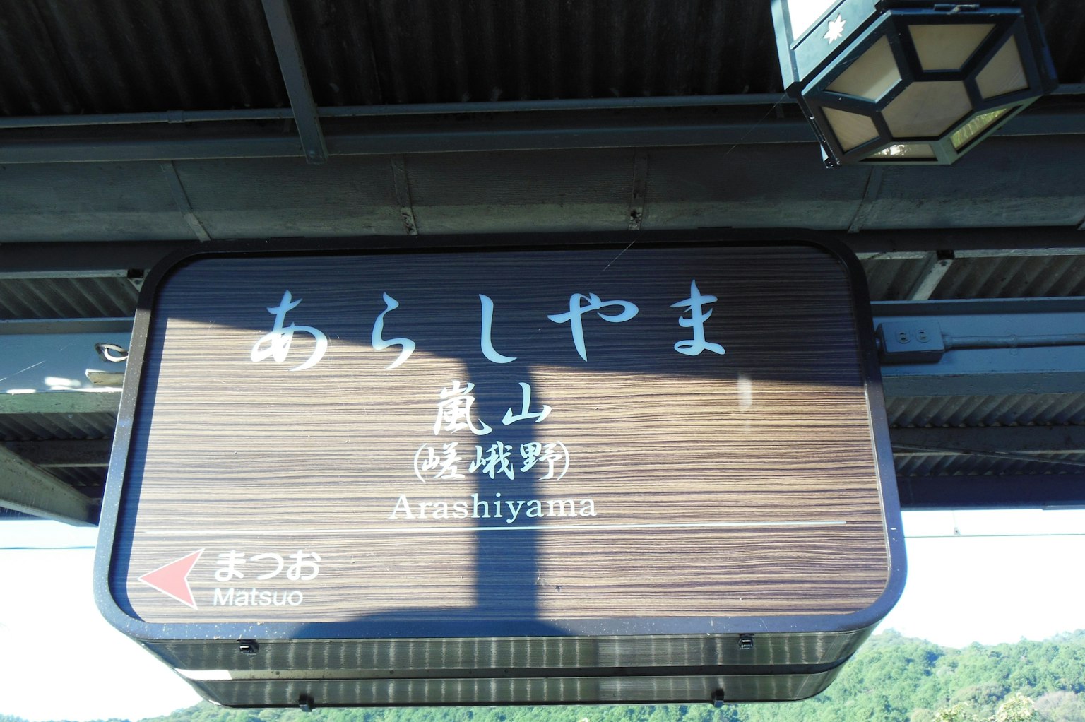 ป้ายไม้ที่สถานีอาราชิยามะแสดงชื่อสถานีเป็นภาษาญี่ปุ่นและอังกฤษ