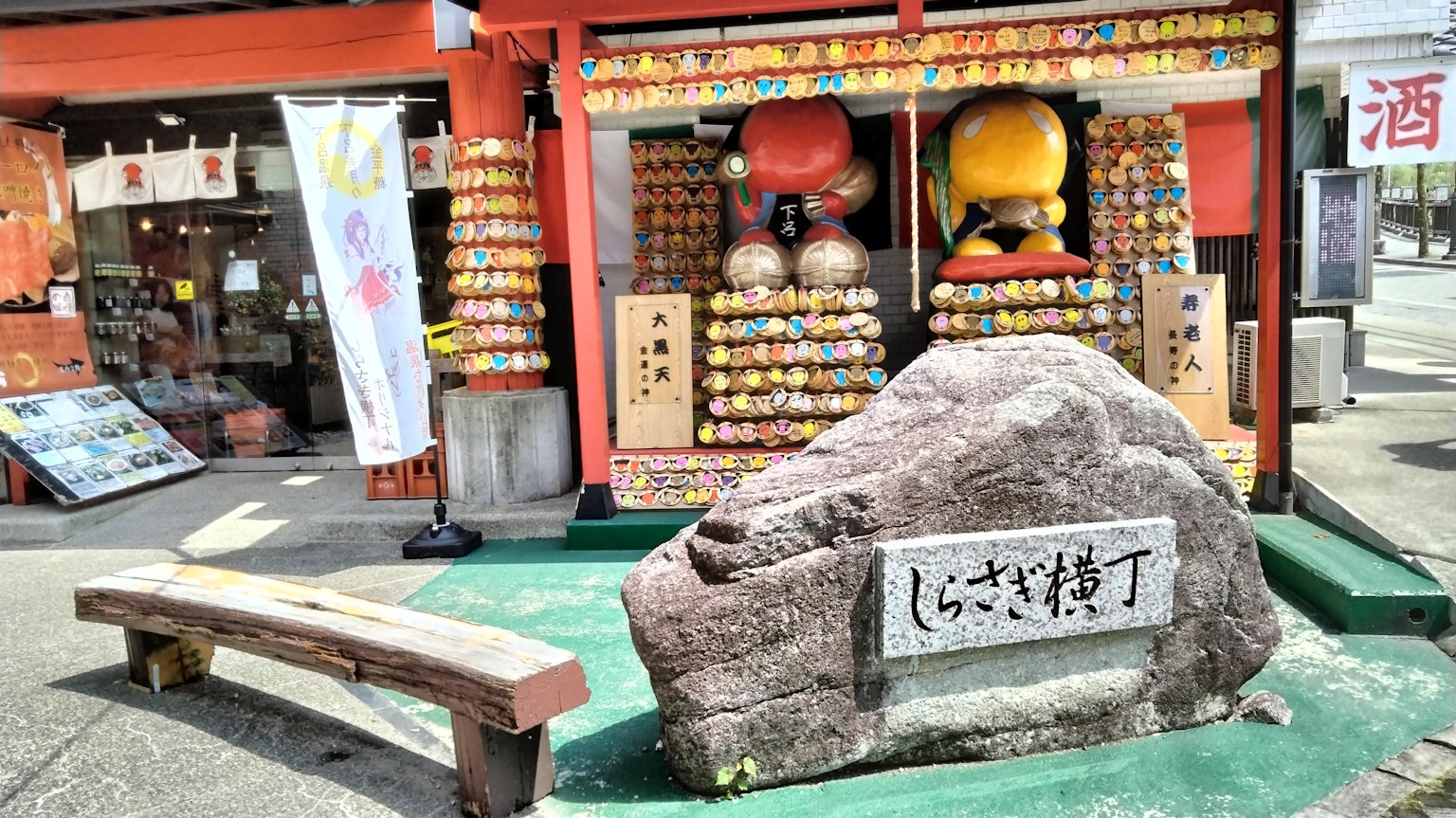 Scène vibrante d'une rue commerçante japonaise avec une grande pierre portant des inscriptions et des décorations colorées